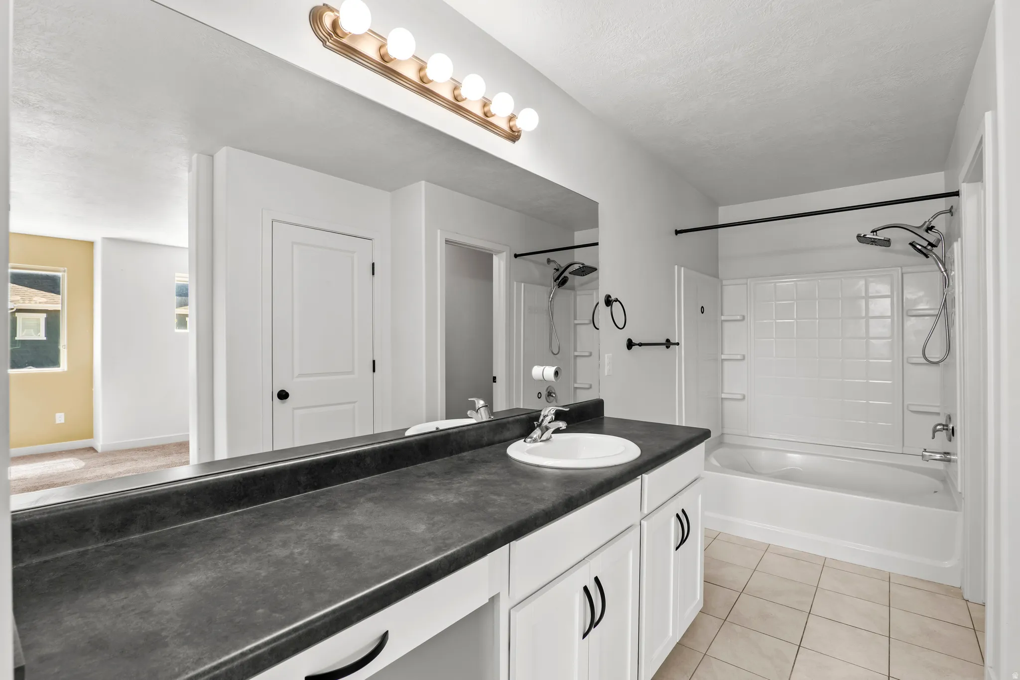 Contemporary bathroom featuring a large vanity with white cabinetry, dark countertop, and an integrated sink