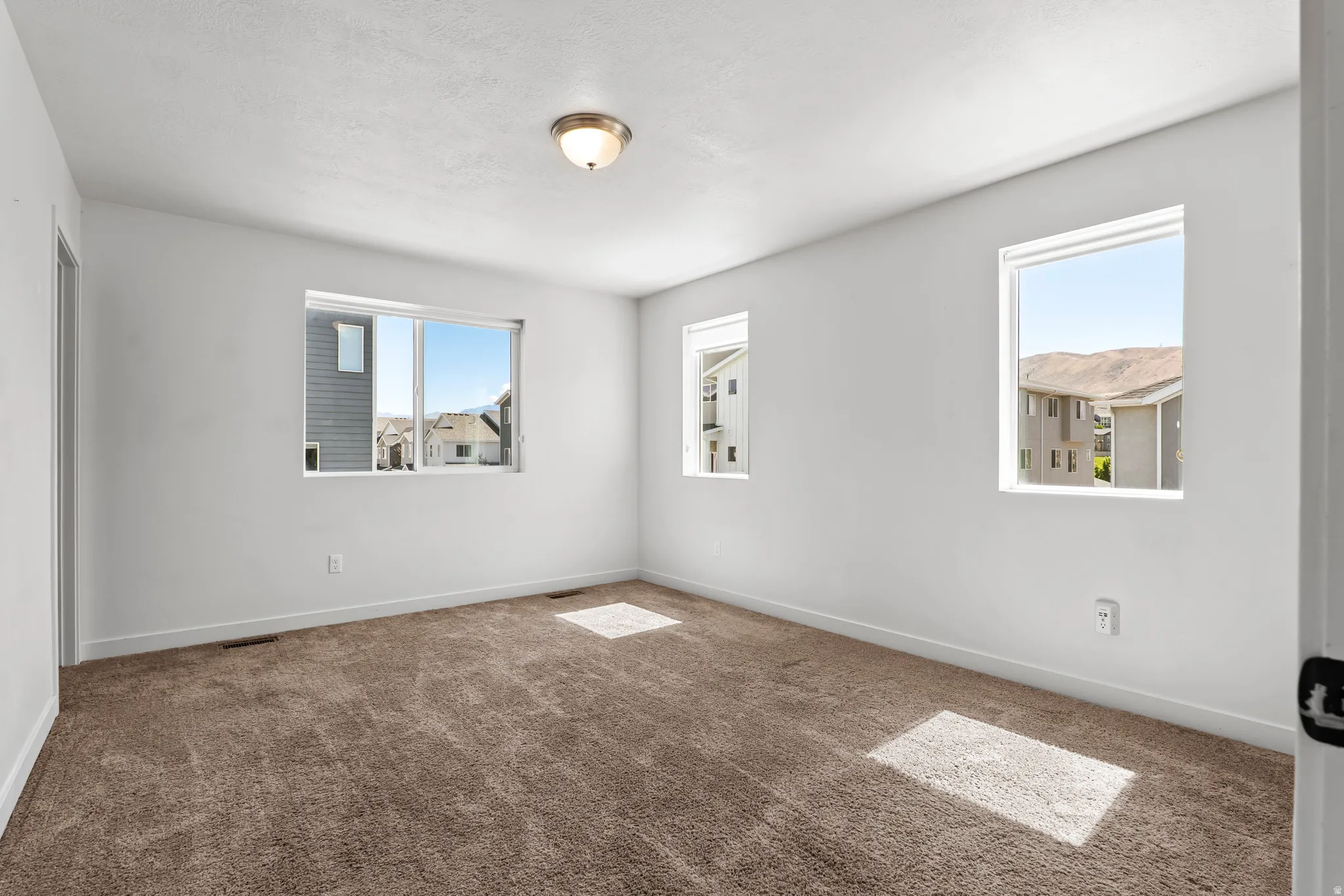 Spacious room featuring neutral carpeting, multiple windows for natural light, white walls, white baseboards, and a ceiling-mounted light fixture