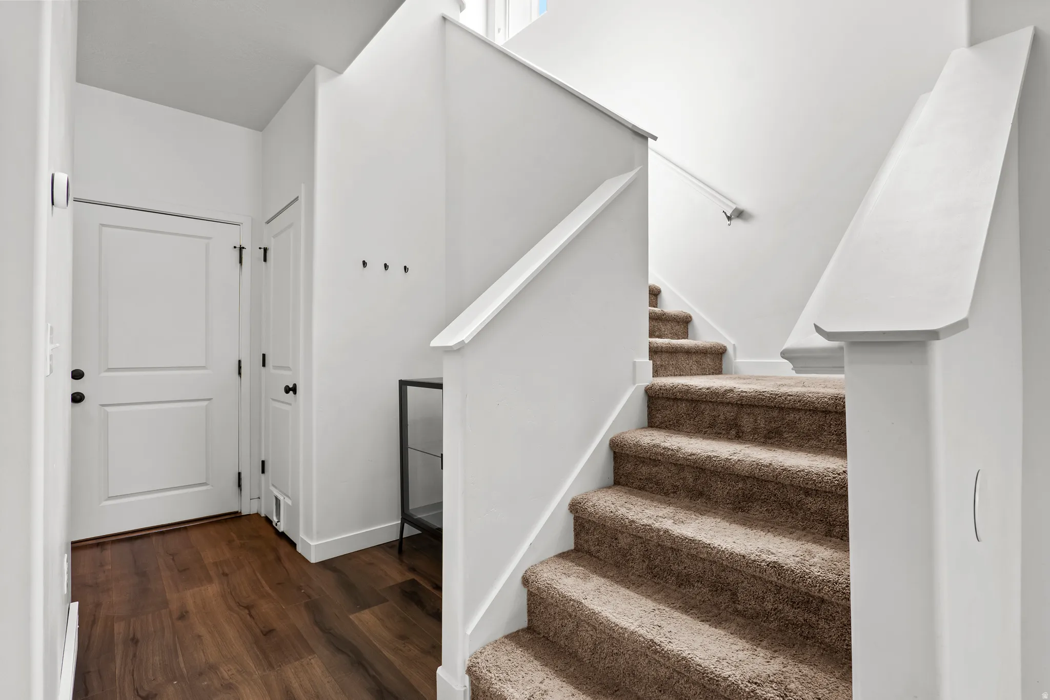 Foyer featuring wood-finish flooring, white panel doors, and a carpeted staircase with white railings