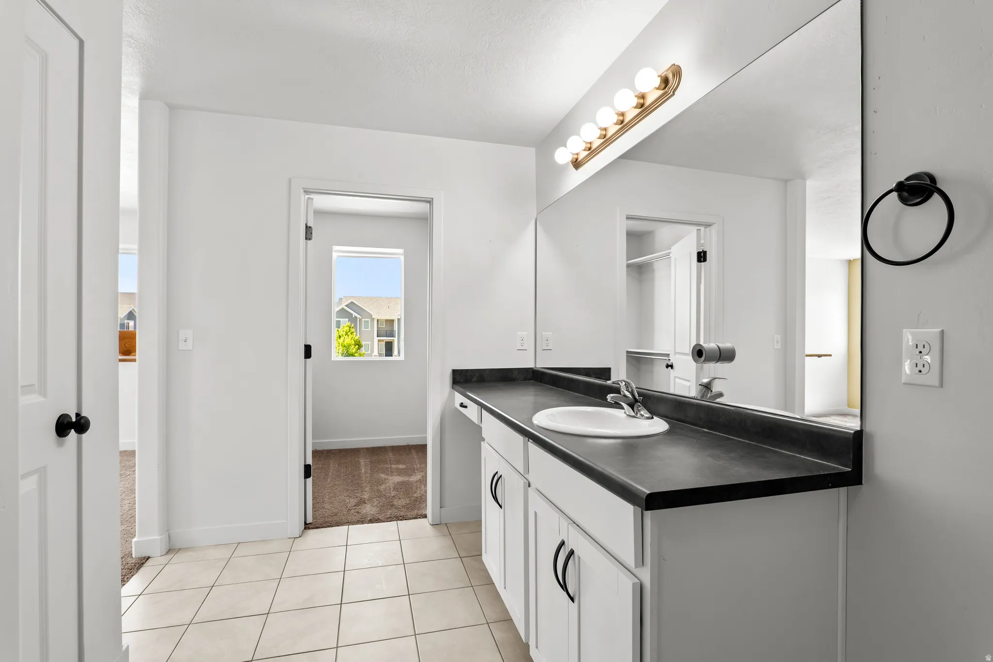 Bathroom vanity featuring a single basin sink, dark countertop, and white cabinetry with black hardware