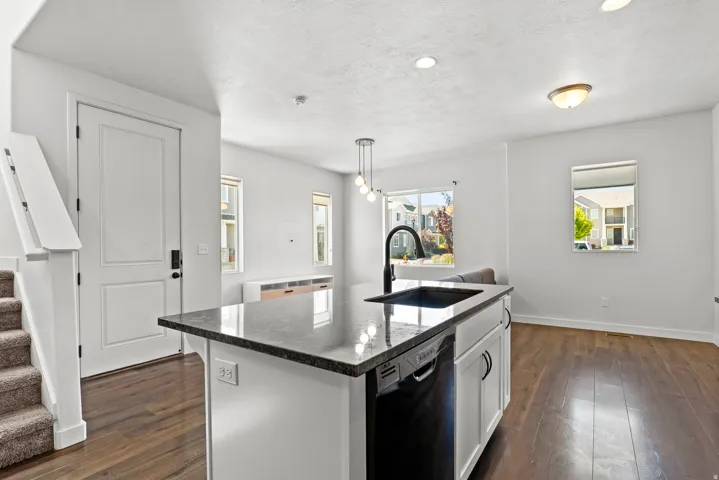 Kitchen island featuring a dark countertop, an undermount sink with a gooseneck faucet, and integrated dishwasher