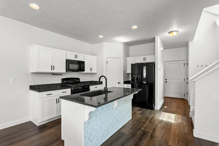 Kitchen featuring white cabinetry, dark stone countertops, a central island with a tiled base, and wood-finish flooring