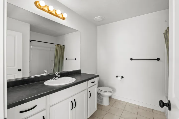 Bathroom featuring a single vanity with white cabinetry, dark countertop, and an oval undermount sink