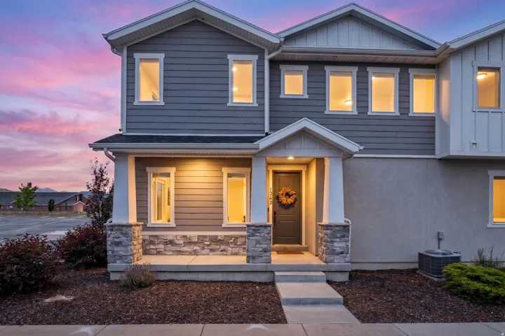 Contemporary multi-level exterior with mixed material facade, featuring a covered porch entrance with stone veneer columns, horizontal siding, and board-and-batten accents