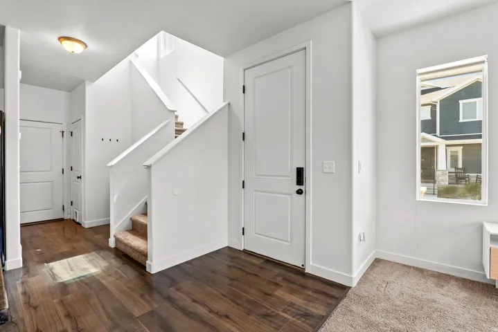 Entryway featuring wood-finish flooring, white walls, and a carpeted staircase