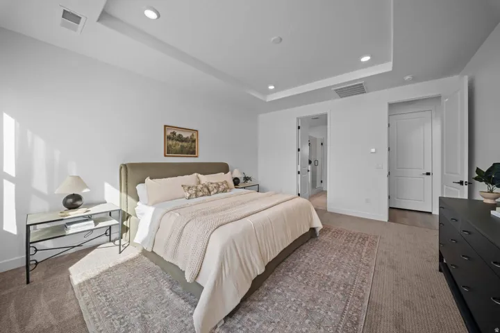 Recessed lighting illuminating a spacious room with a tray ceiling and plush carpet flooring