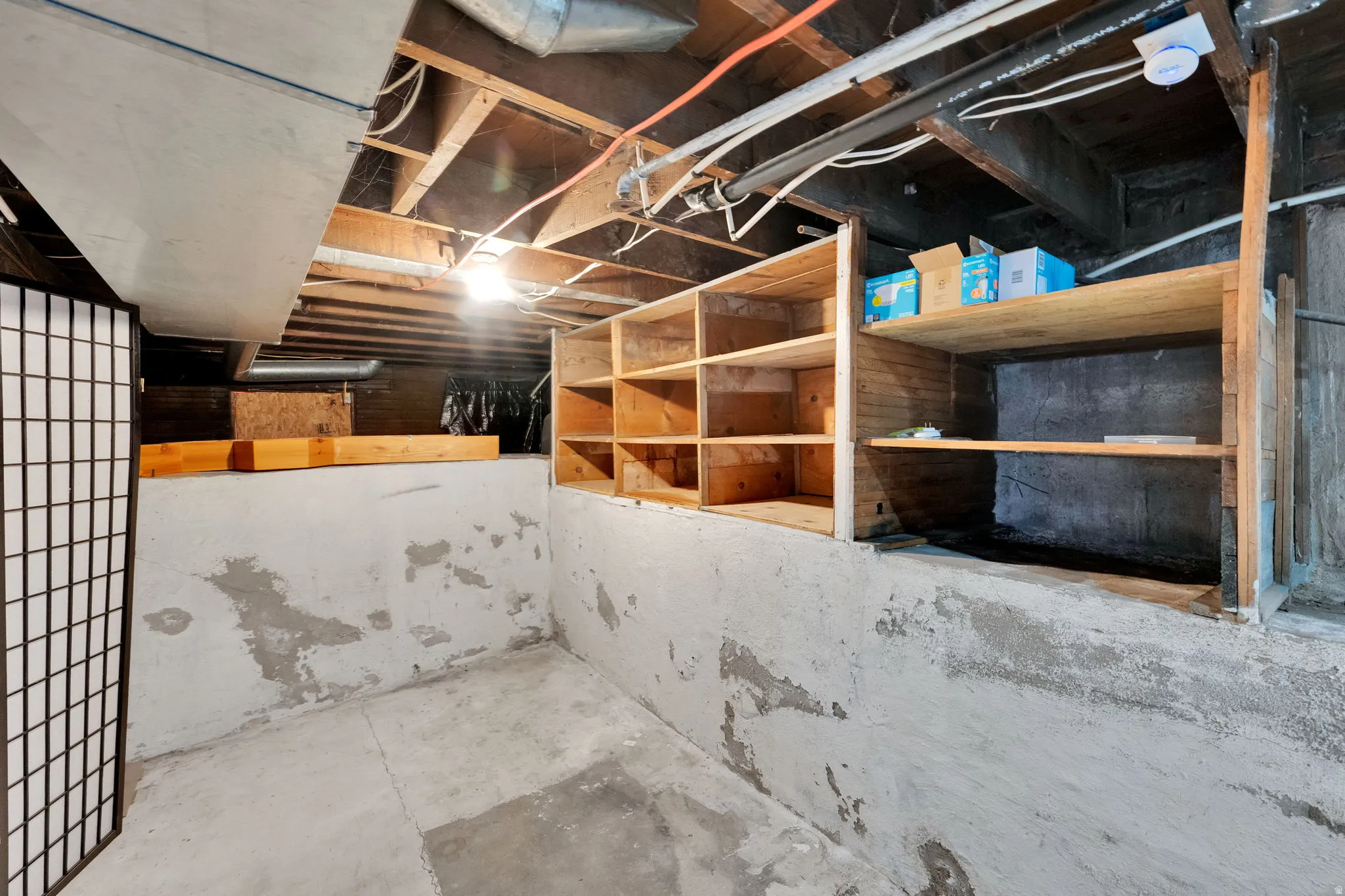 Unfinished basement featuring exposed wood joists, concrete flooring, built-in wooden shelving, and visible ductwork