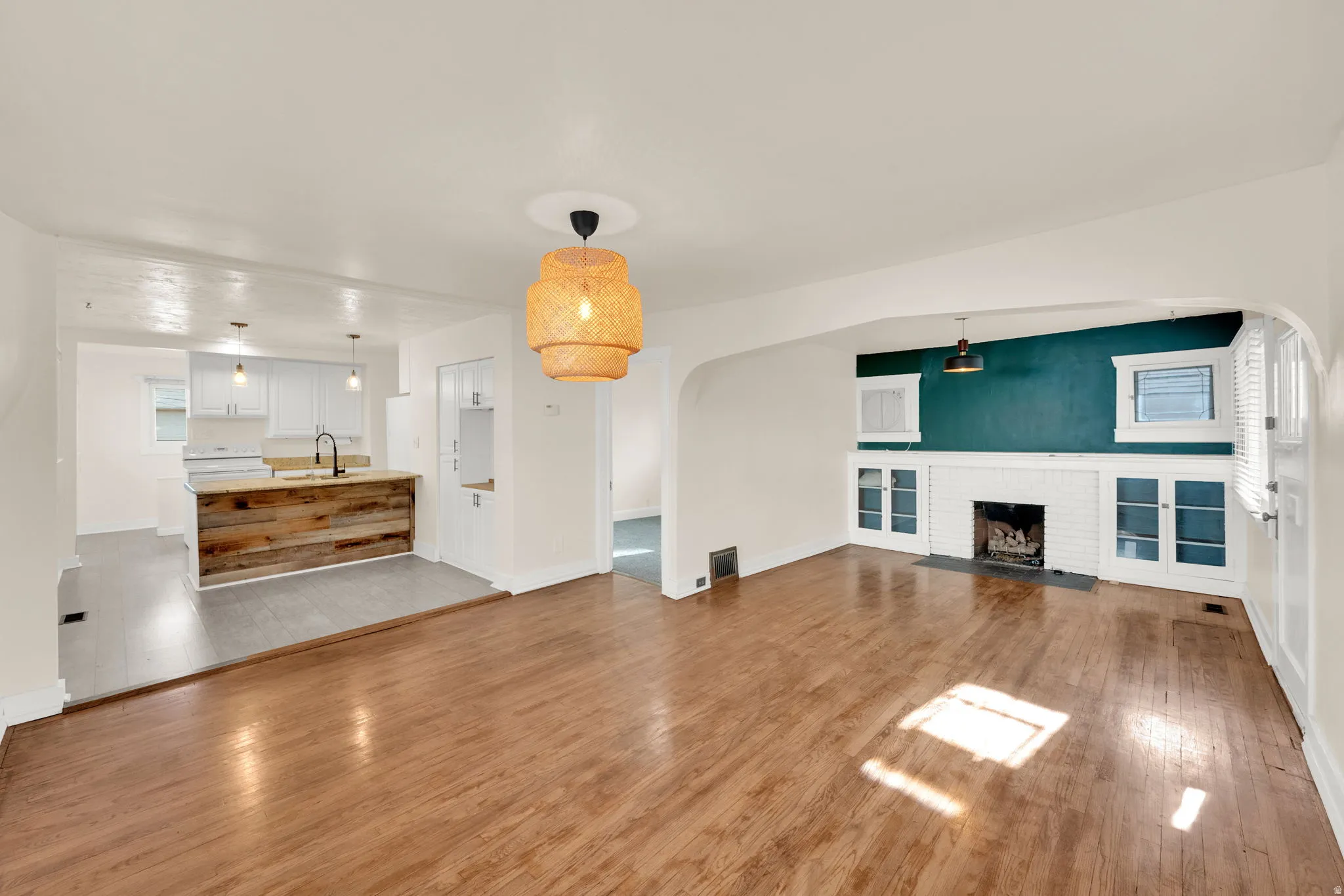 Hardwood flooring extending into an arched doorway, featuring a white brick gas fireplace with built-in cabinetry, and a kitchen with a wood-clad island and white cabinetry