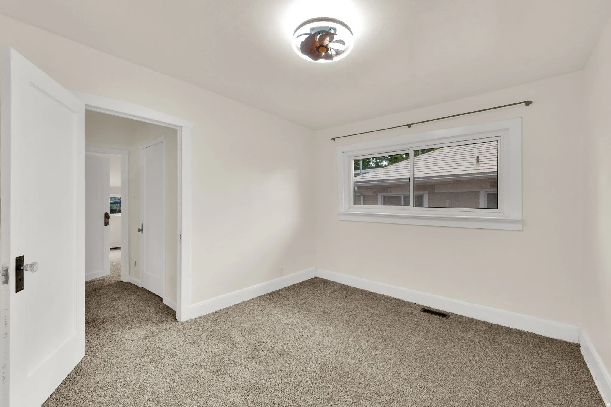 Neutral tone wall paint, light-colored carpet flooring, white trim, single window, and a ceiling light fixture