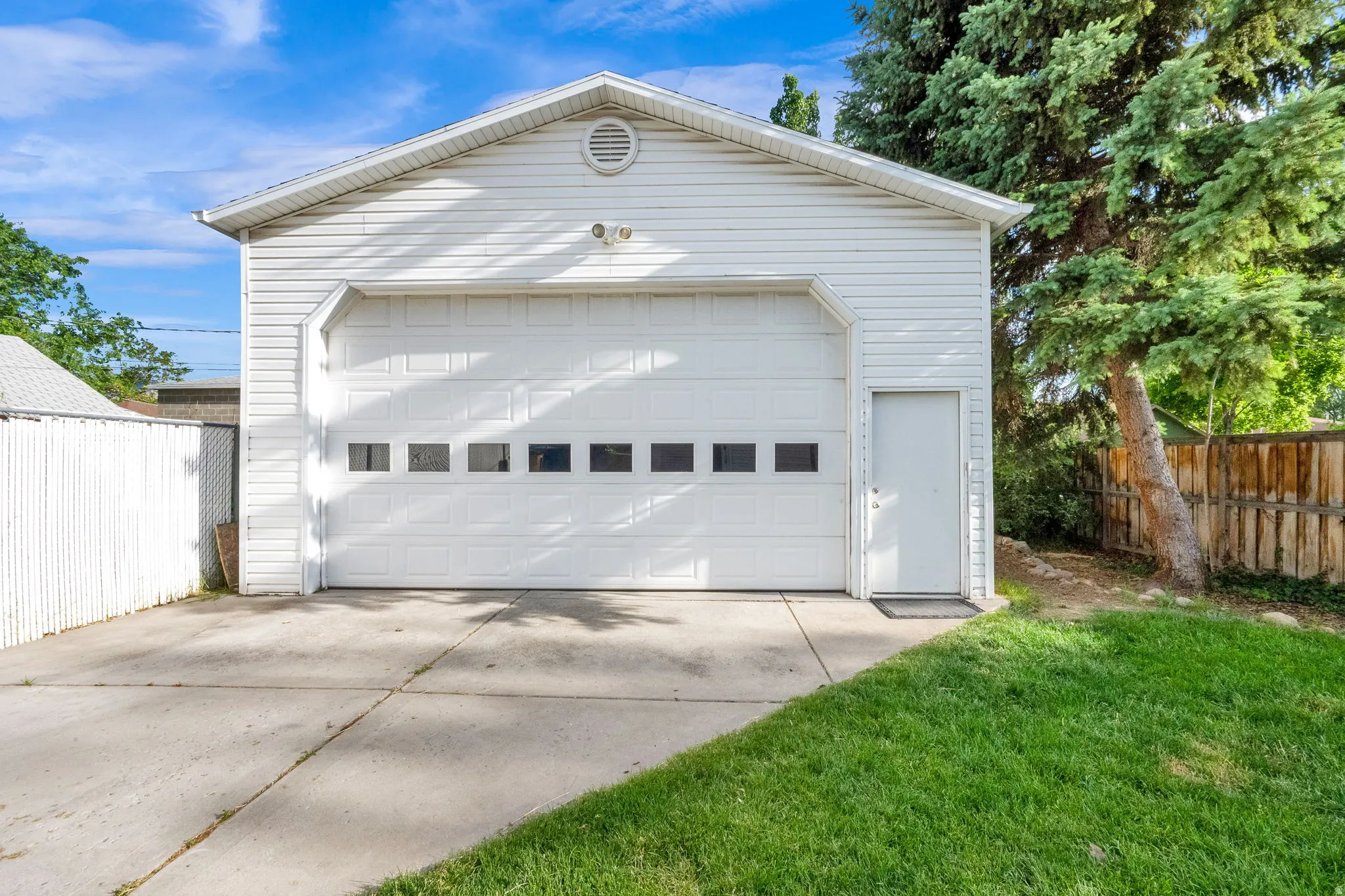 Detached garage with white vinyl siding and a single overhead door featuring transom-style windows