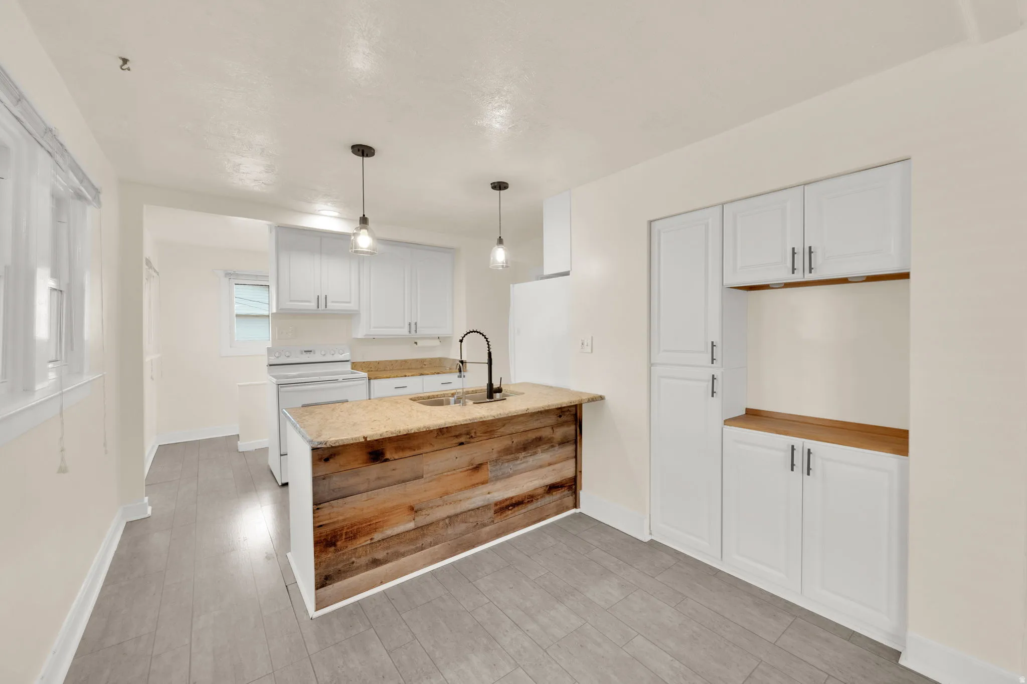 Kitchen featuring a wood-finish island with a stone countertop and integrated sink, white shaker-style cabinetry, a white electric range, and wood-finish flooring