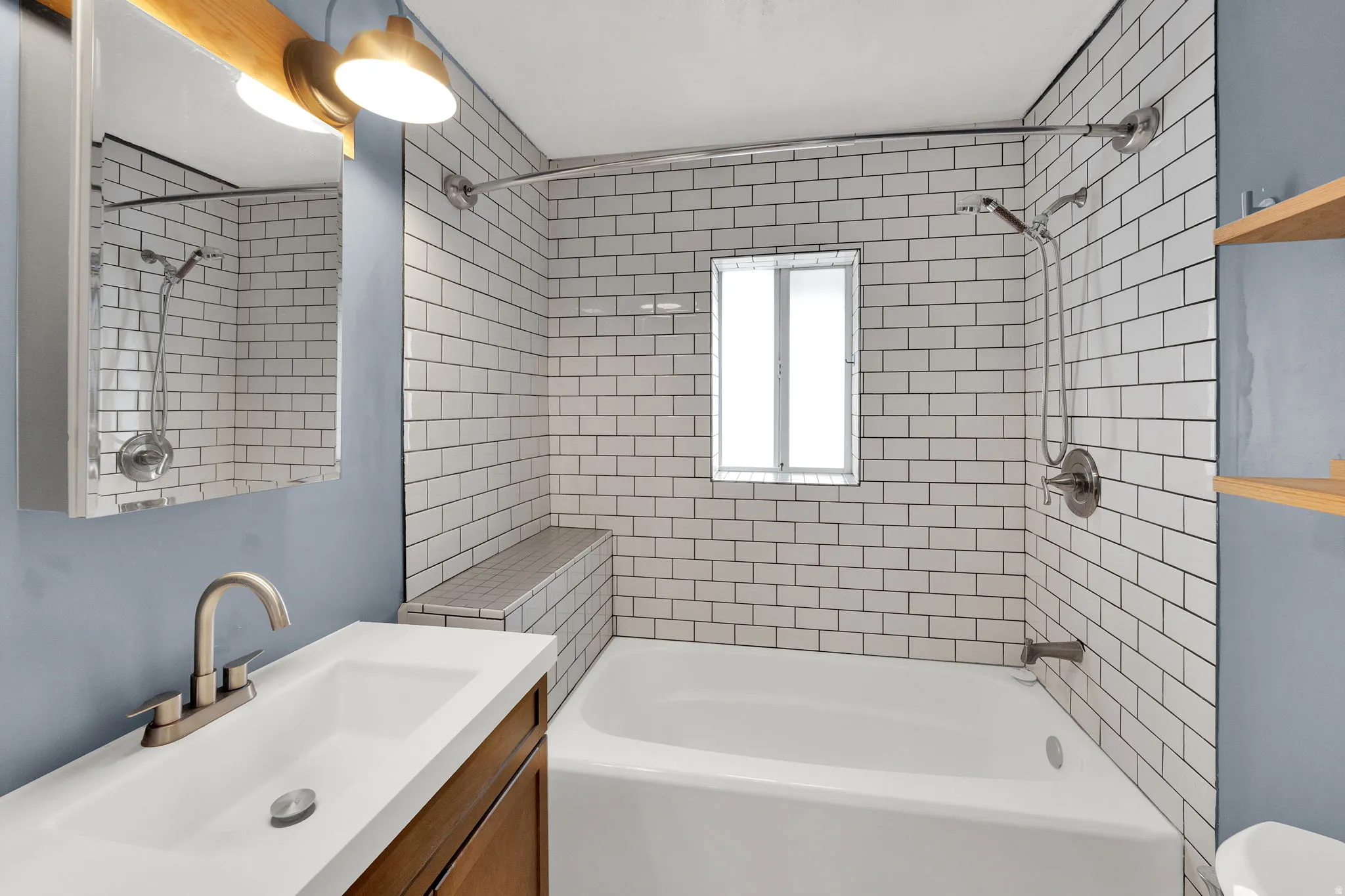 Bathroom featuring a white subway tile shower surround with a built-in bench, a window, a white bathtub, and a vanity with a rectangular sink and brushed nickel faucet