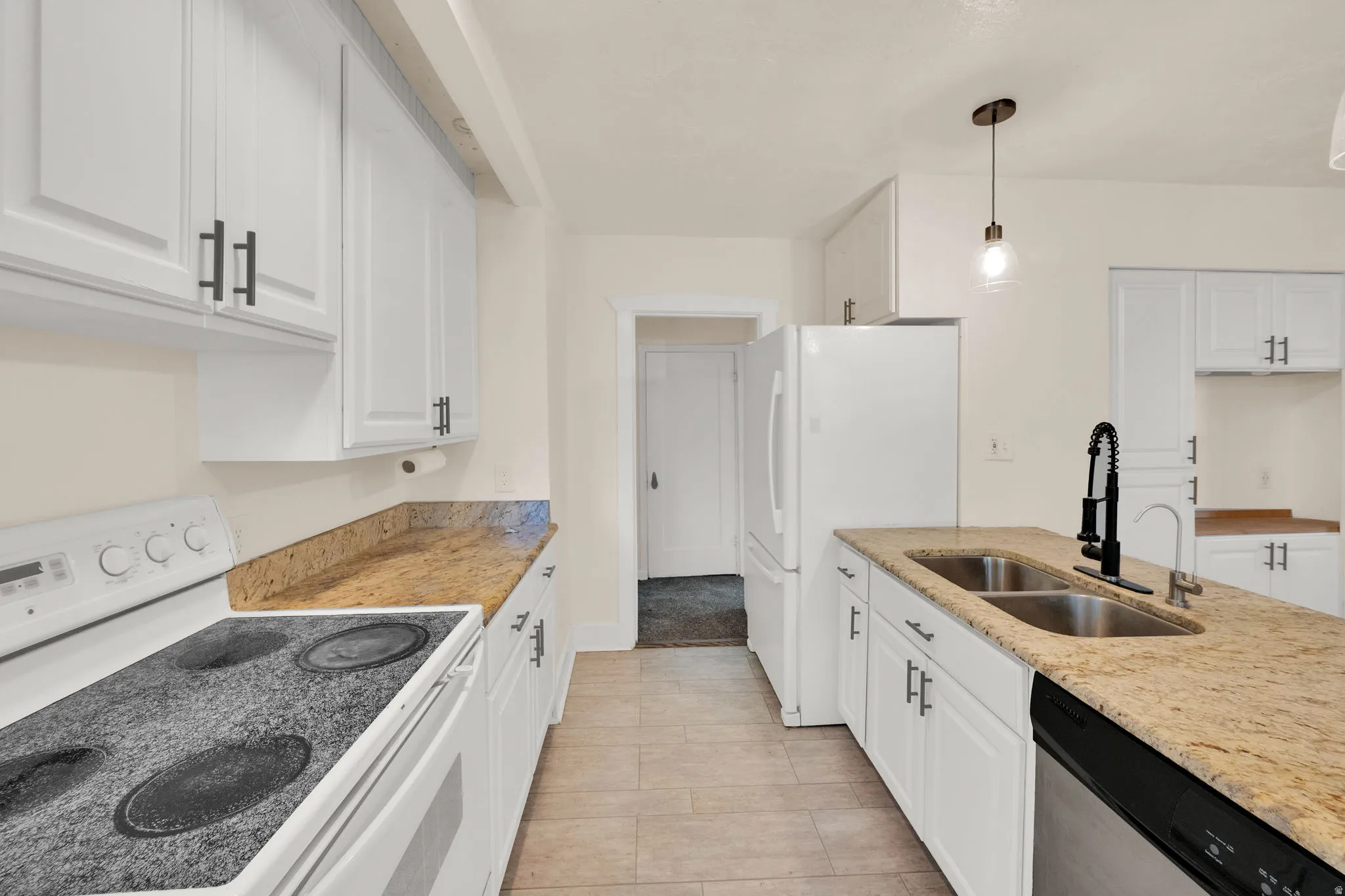 Kitchen featuring white cabinetry with dark hardware, granite-style countertops, stainless steel double basin sink with a matte black faucet, and tile flooring