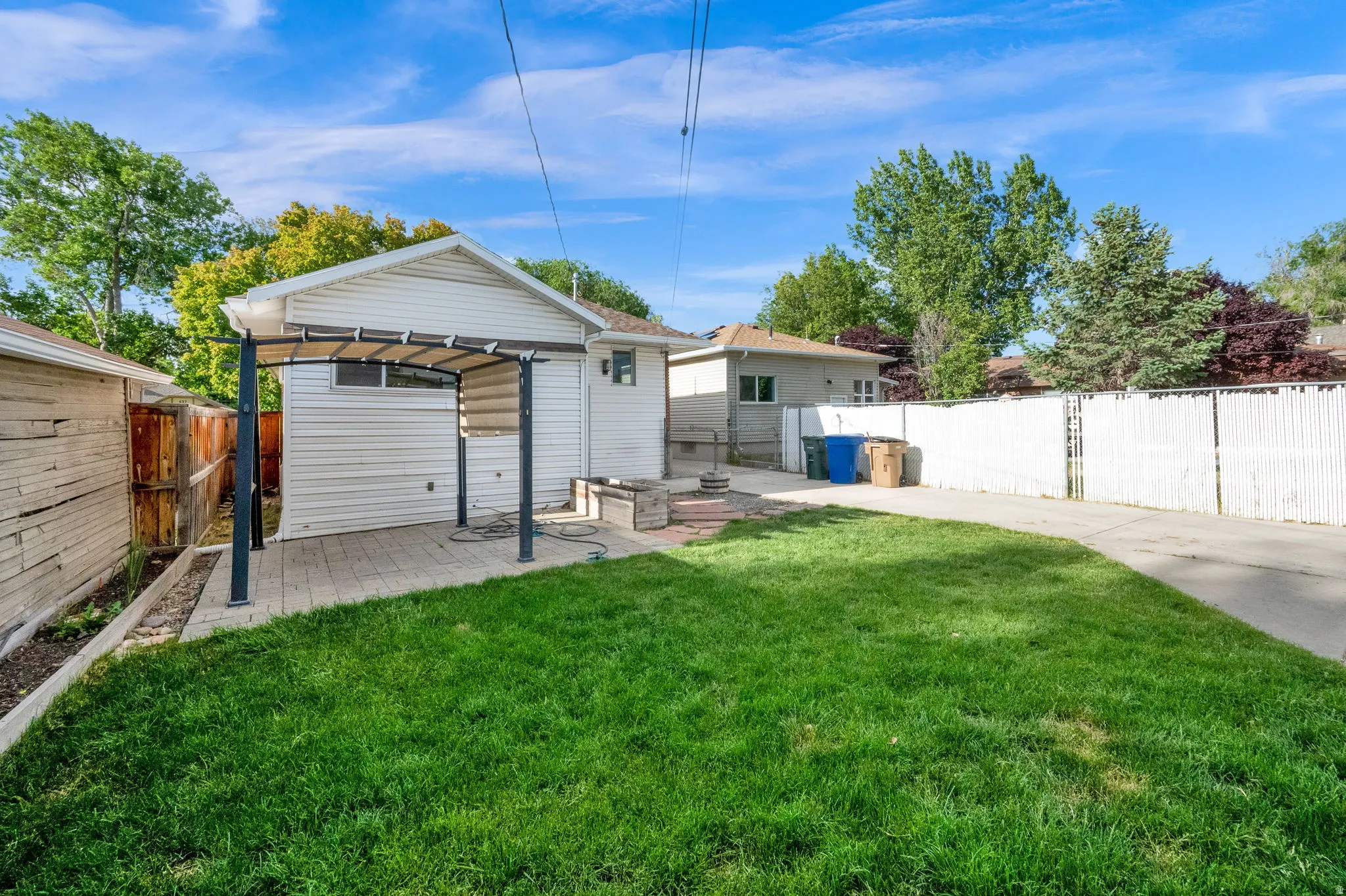 Expansive backyard featuring a manicured lawn, paver patio, metal pergola structure, and a white privacy fence