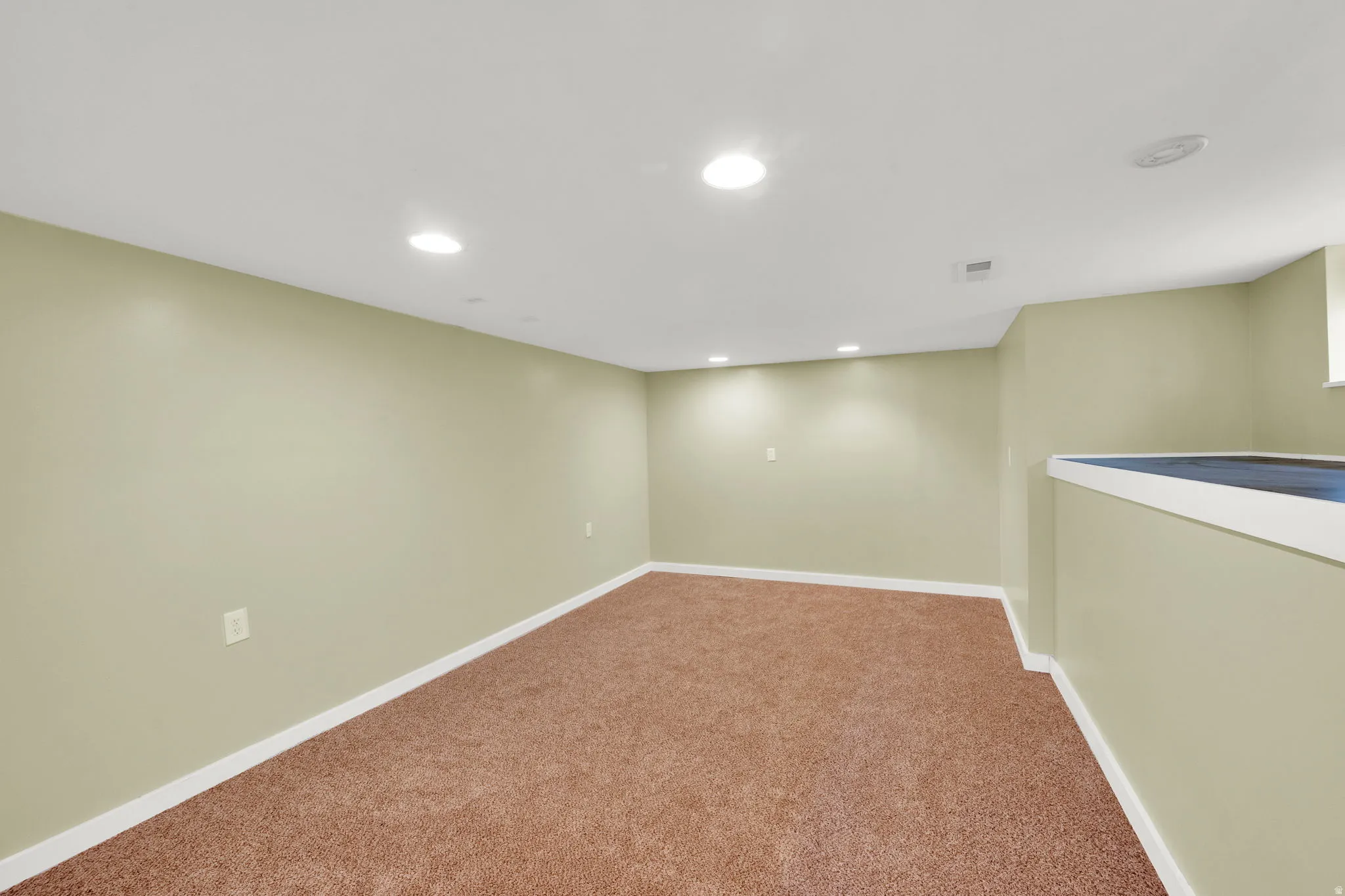 Carpeted room with recessed lighting, light green painted walls, white trim, and a partial wall feature with a white cap