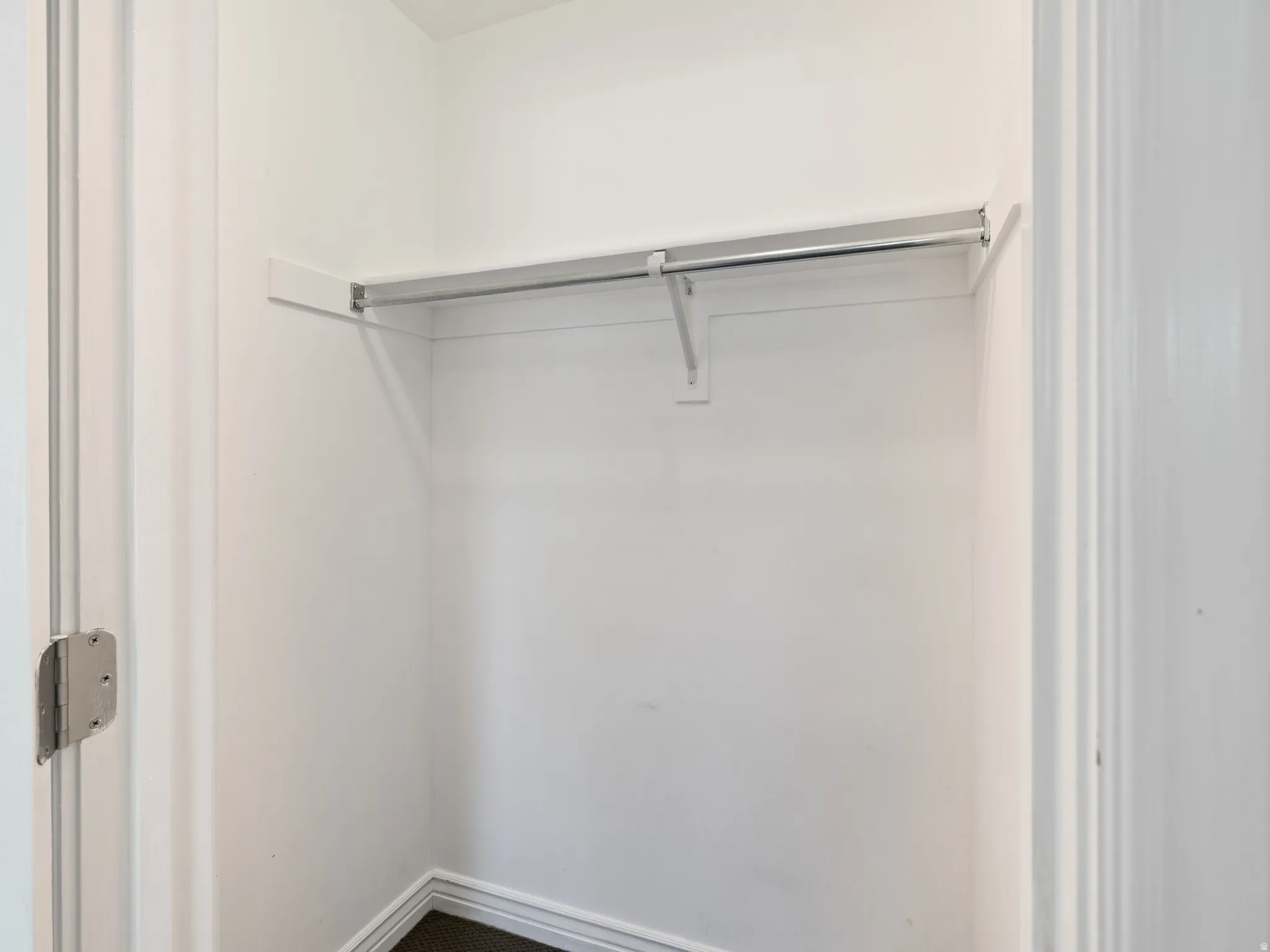 Interior closet featuring a single hanging rod, upper shelf, white painted walls, and dark flooring