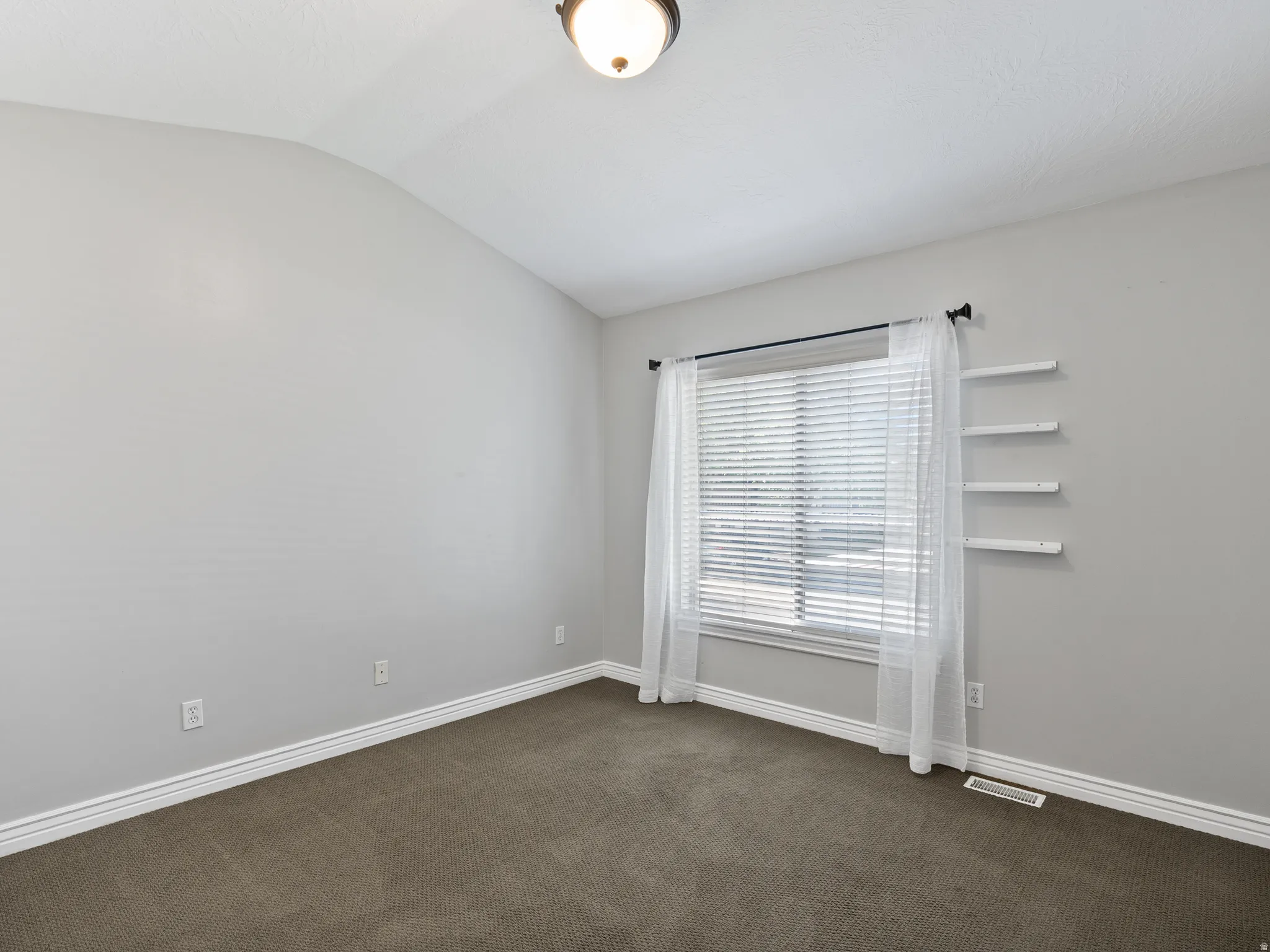 Carpeted room featuring light gray walls, white baseboards, and a window with blinds and sheer curtains