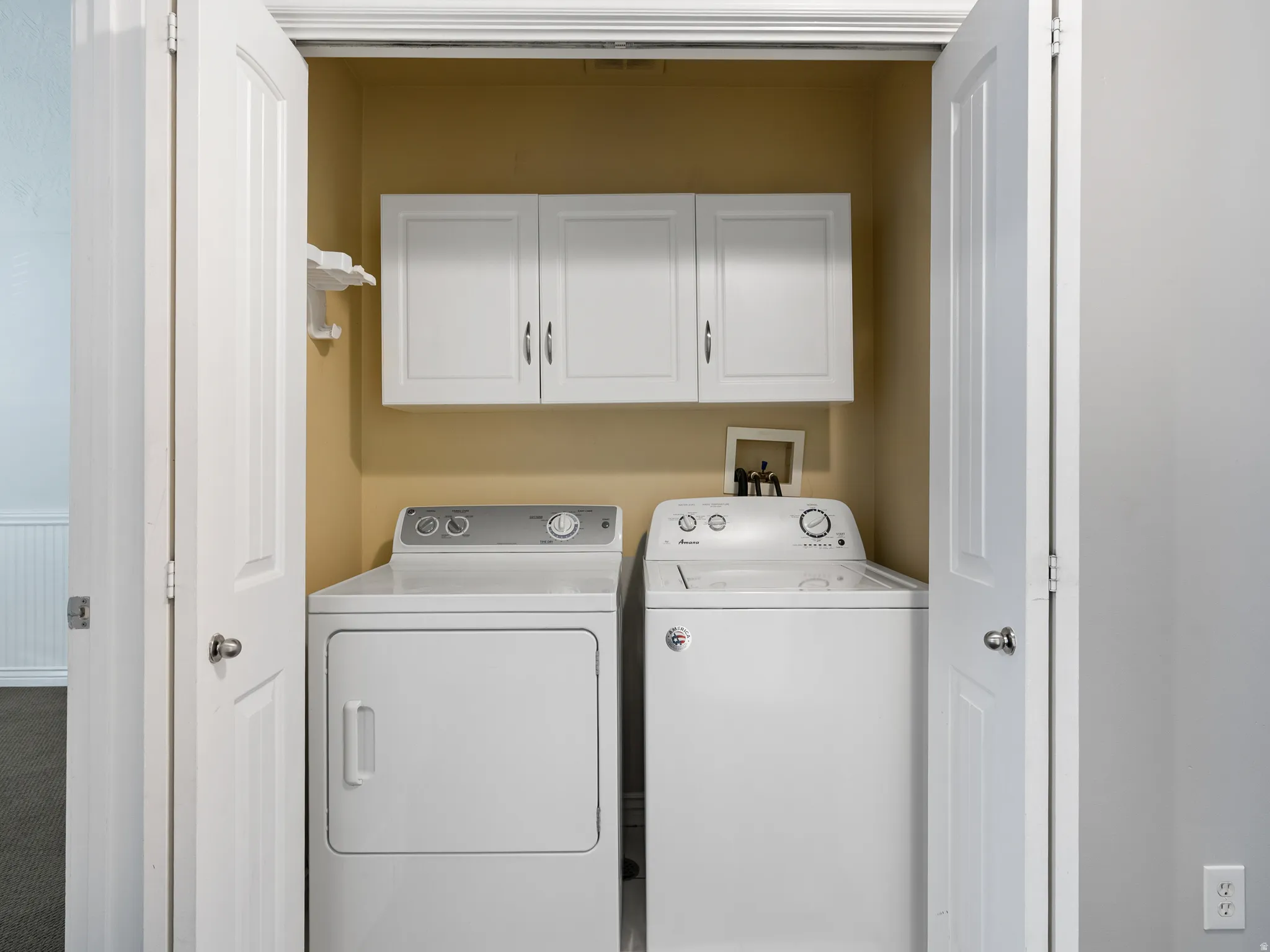 Dedicated laundry closet featuring a top-load washer and front-load dryer, upper white cabinetry, and a white wall-mounted shelf