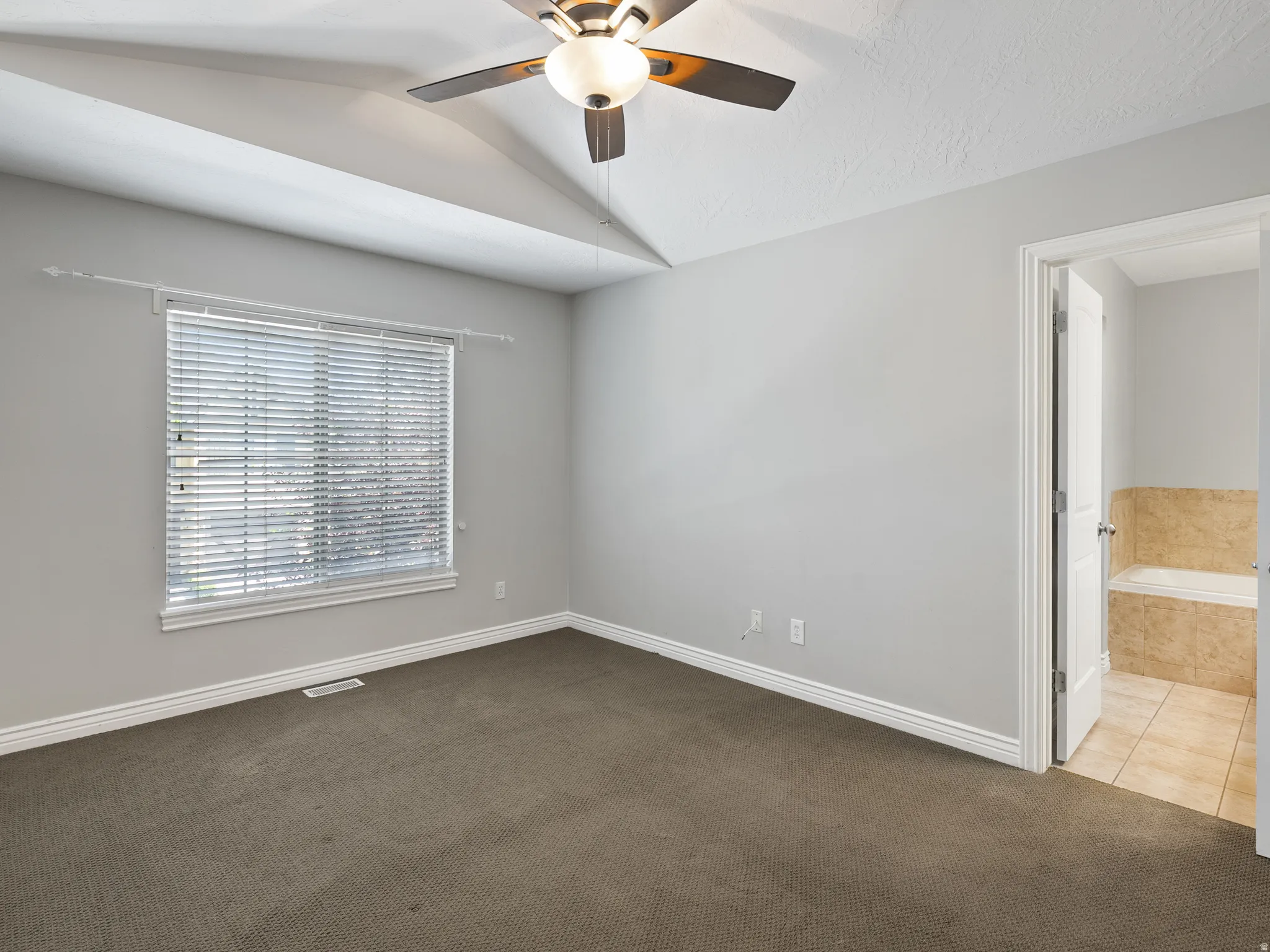 Spacious room featuring vaulted ceilings, a ceiling fan with integrated lighting, and neutral-toned wall paint