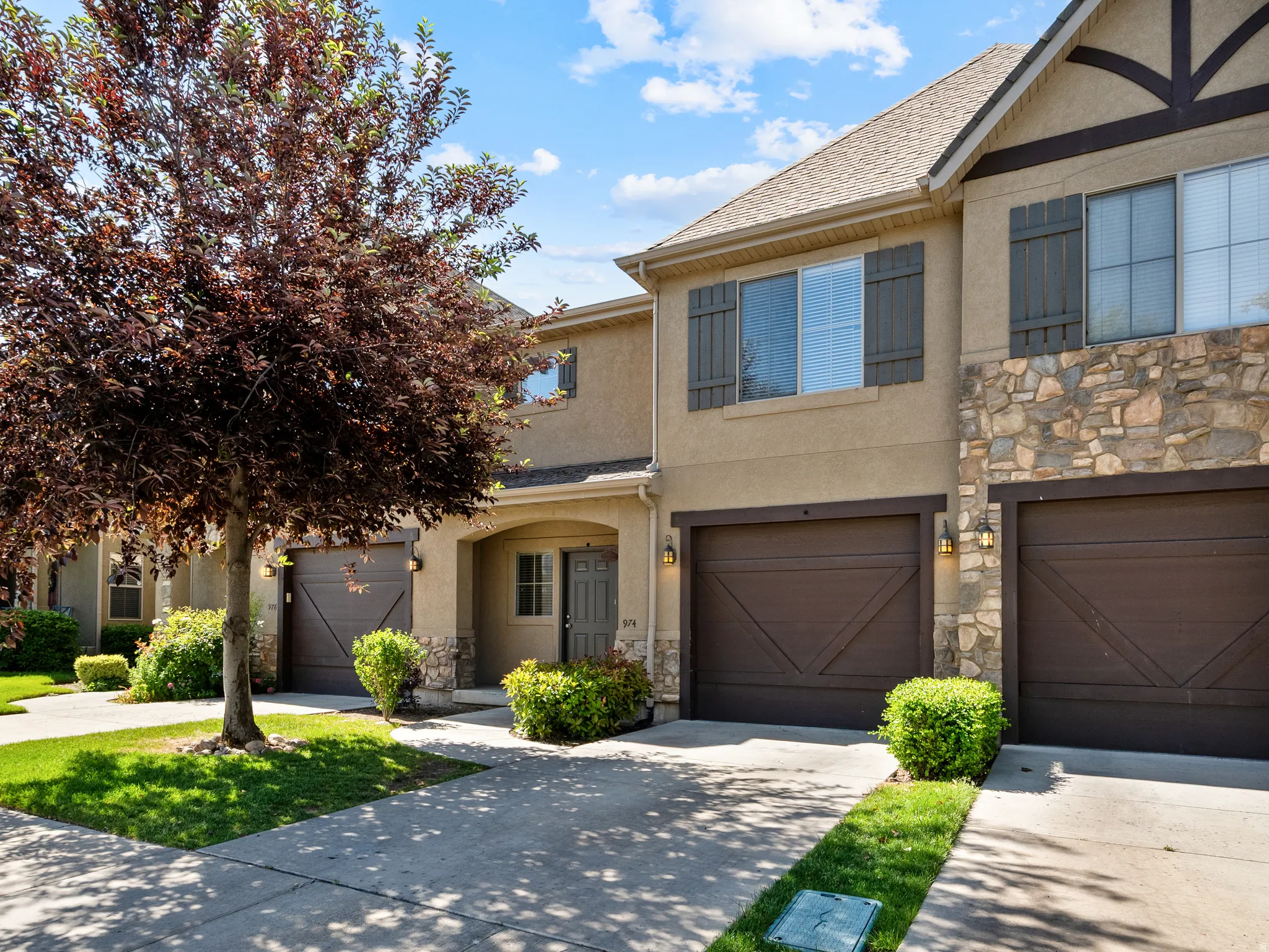 Townhome exterior featuring stone accents, stucco siding, dark wood-style garage doors, and front entry porch