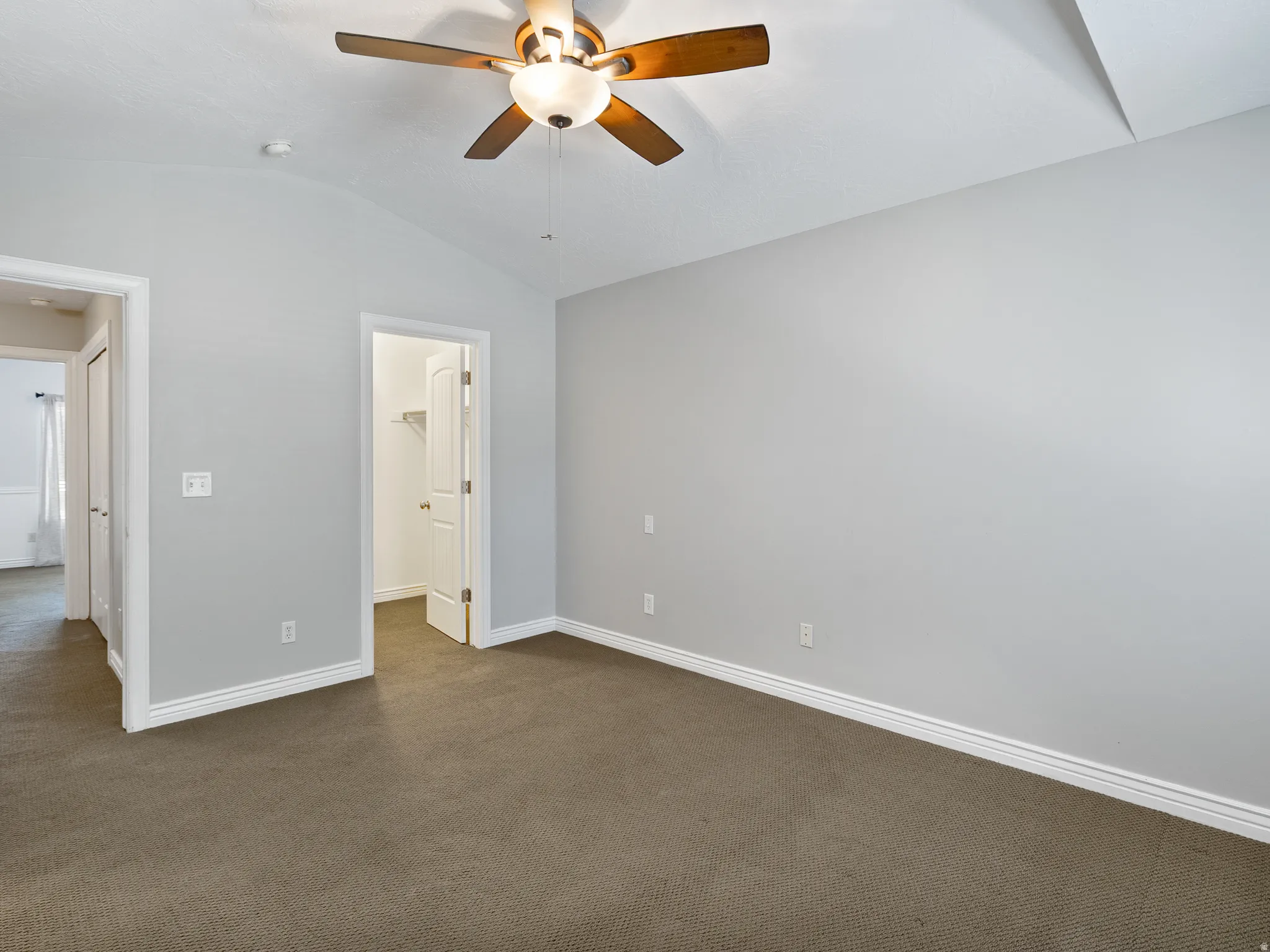 Carpeted room featuring a ceiling fan with integrated lighting, vaulted ceiling, and white baseboards