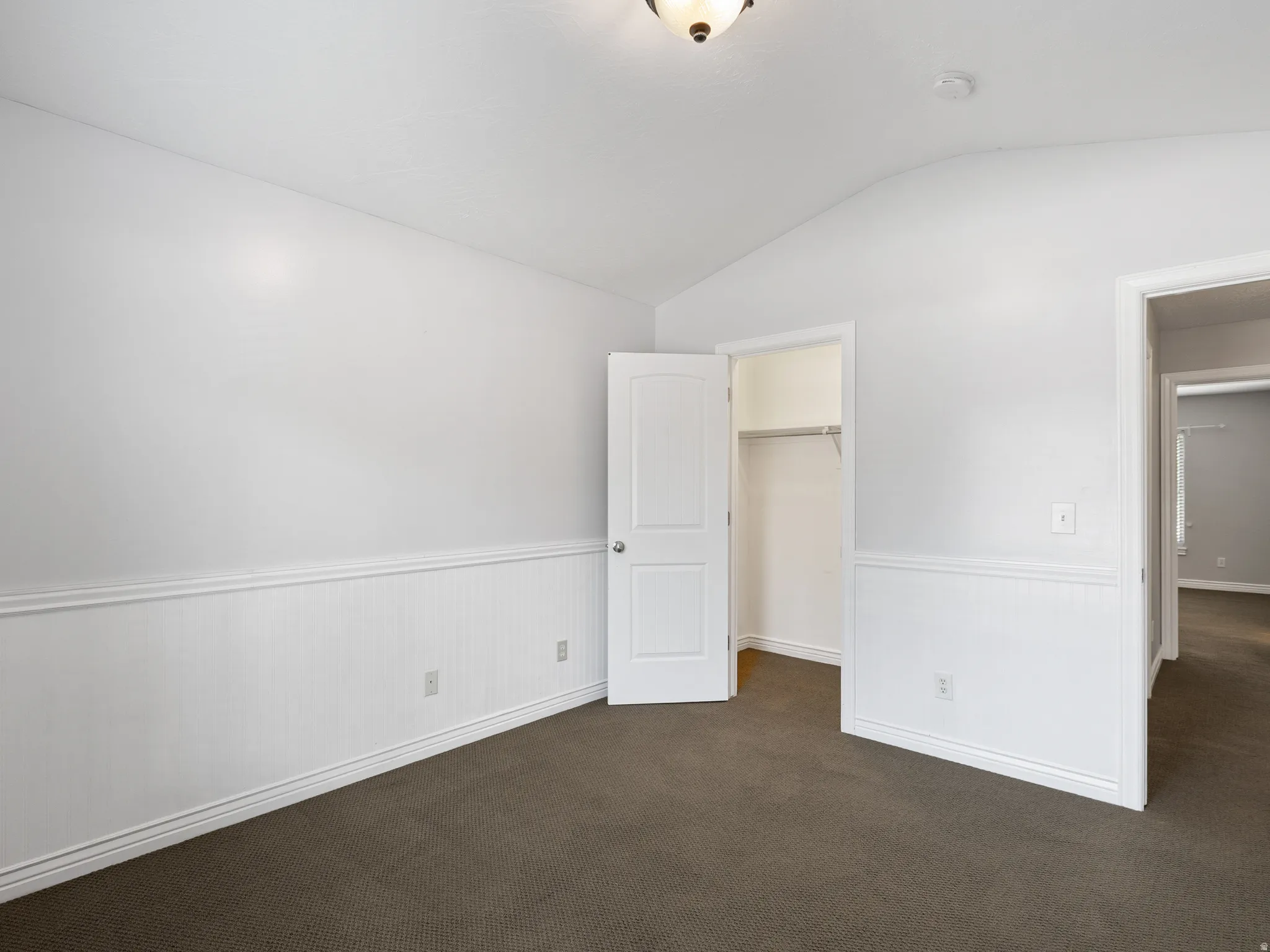 Carpeted room featuring white wainscoting and trim, a two-panel door, and a built-in closet with shelving and hanging rod