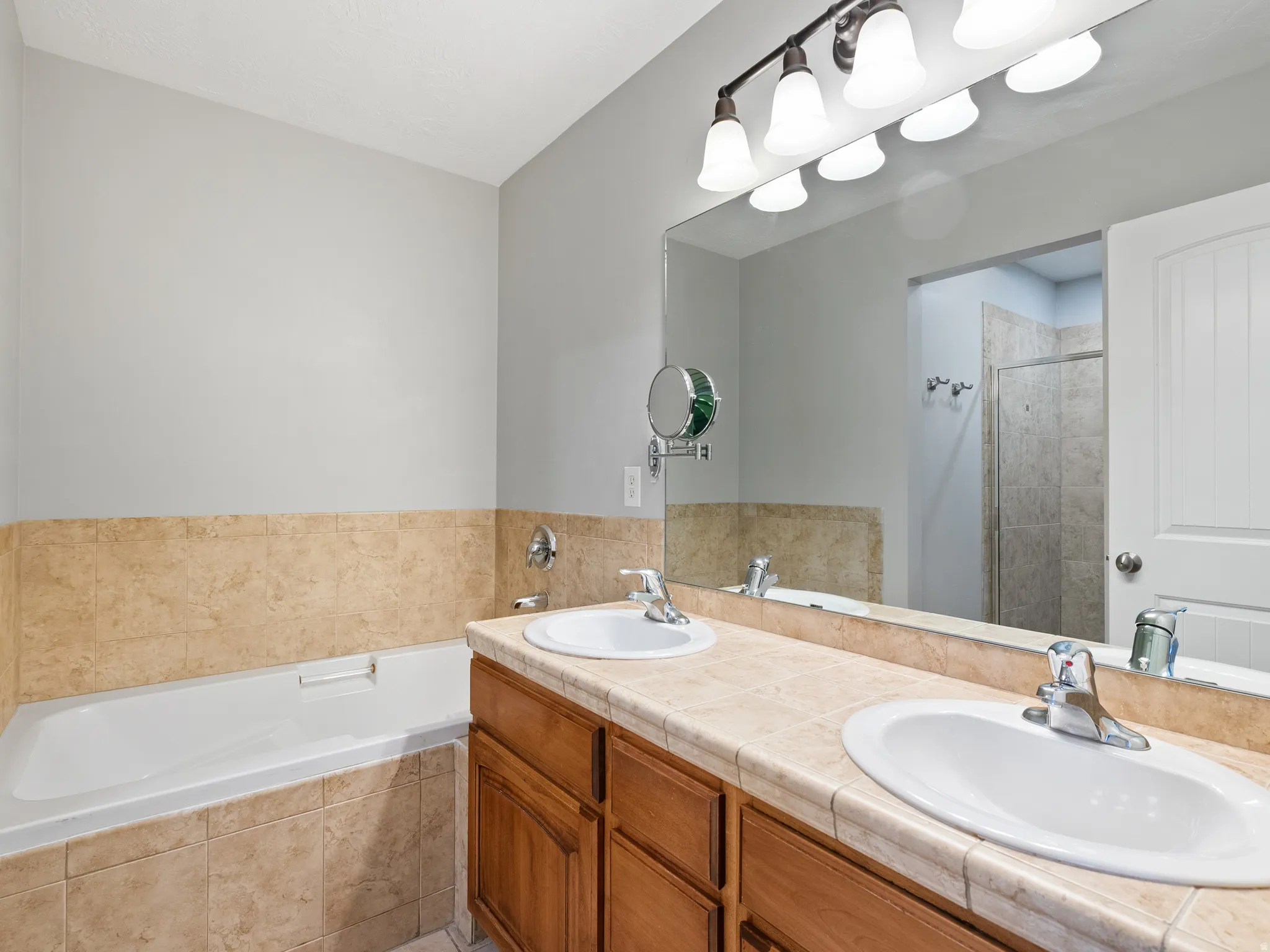Bathroom featuring a dual vanity with light-toned tile countertop, integrated sinks, and wood-finish cabinetry