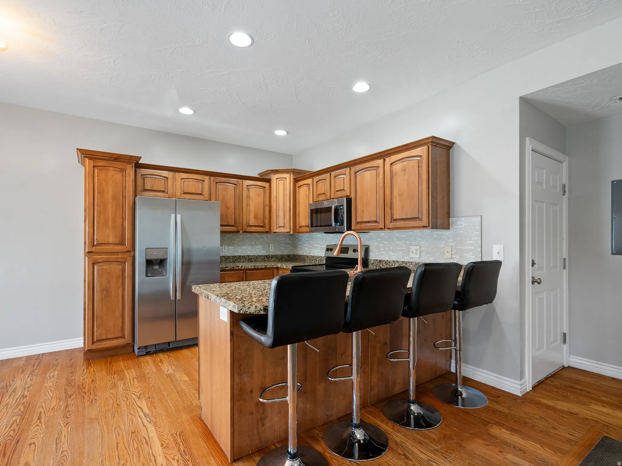 Kitchen featuring wood-finish flooring, recessed lighting, wood cabinetry, stainless steel appliances, and a tiled backsplash