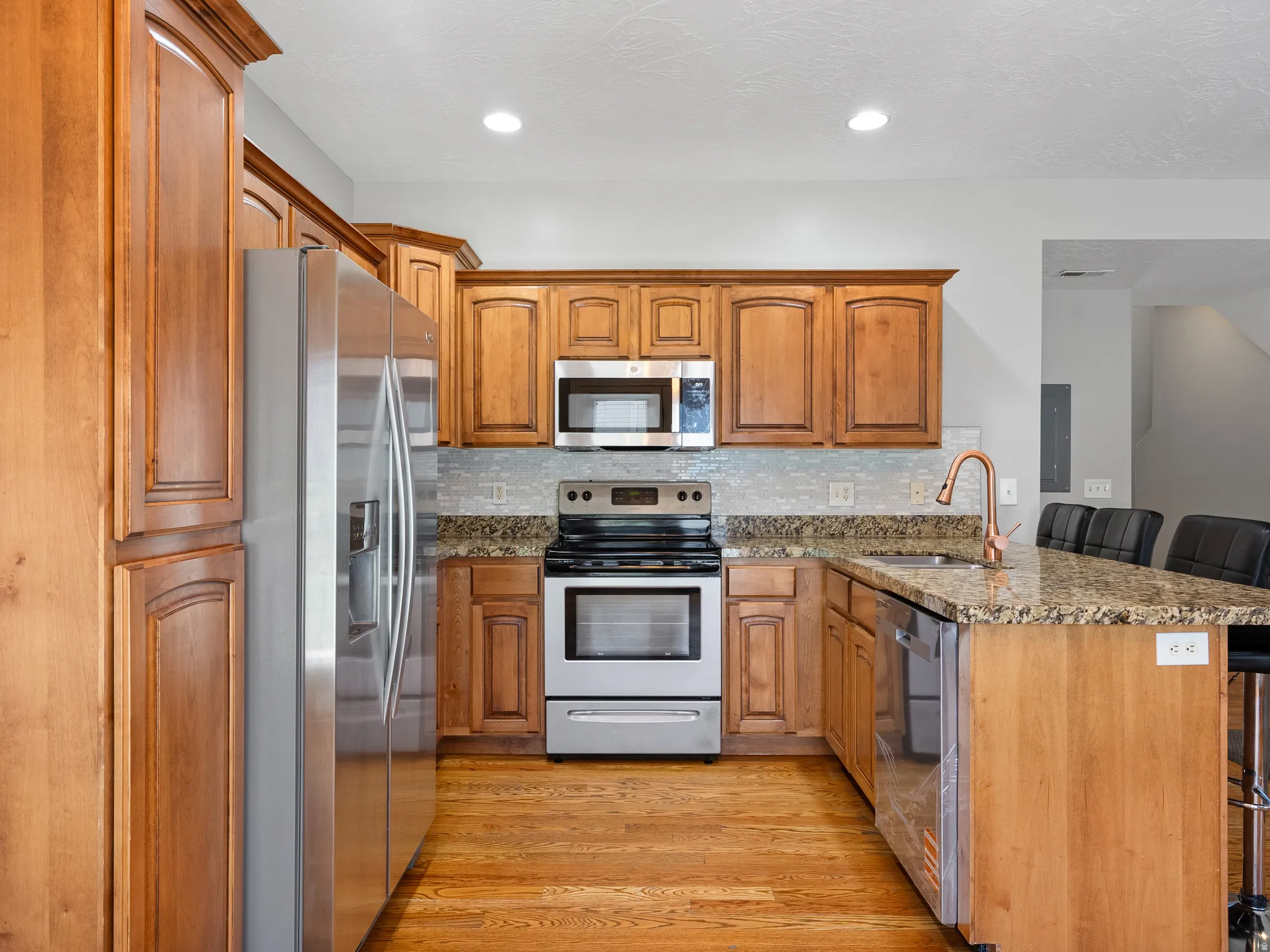 Kitchen featuring wood cabinetry, stainless steel appliances, granite countertops, and wood-finish flooring