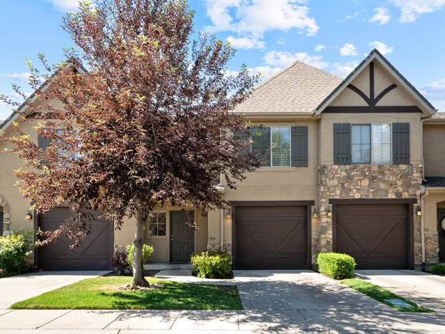 Townhome exterior featuring stone accents, gabled rooflines, dark wood shutters, and two integrated single-car garages with carriage-style doors