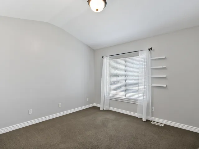 Carpeted room featuring light gray walls, white baseboards, and a window with blinds and sheer curtains