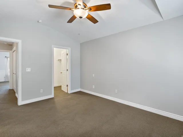 Carpeted room featuring a ceiling fan with integrated lighting, vaulted ceiling, and white baseboards