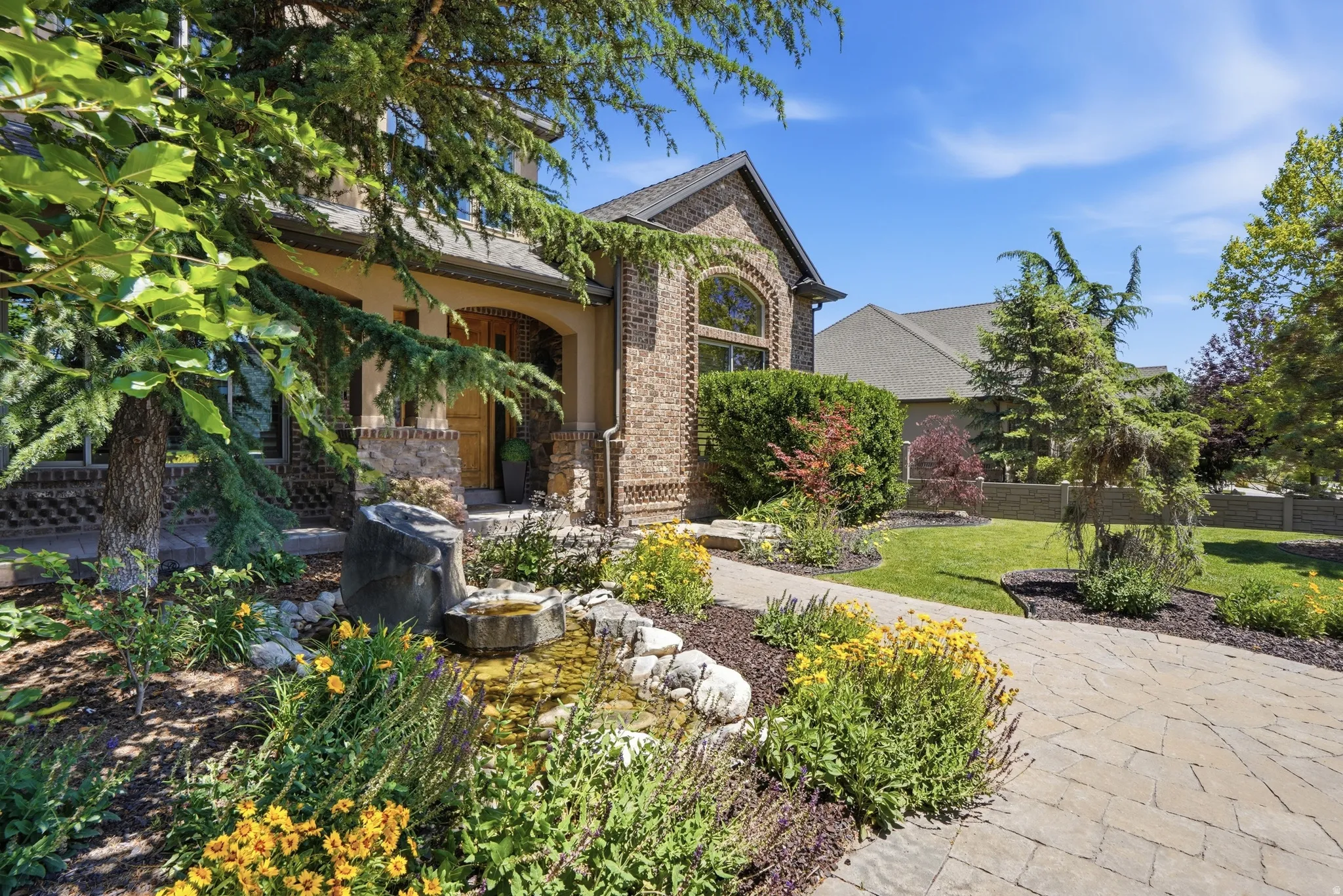 Brick and stucco exterior featuring an arched entryway, detailed window accents, a paver pathway, and a rock-lined water feature