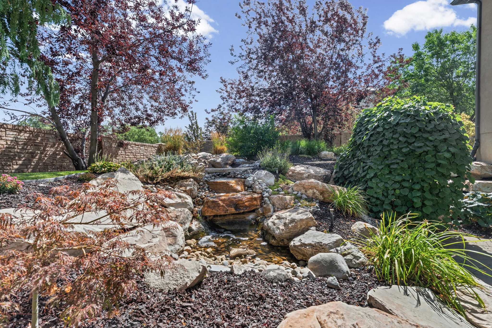 Landscaped backyard featuring a tiered rock water feature, mature trees, and diverse plantings