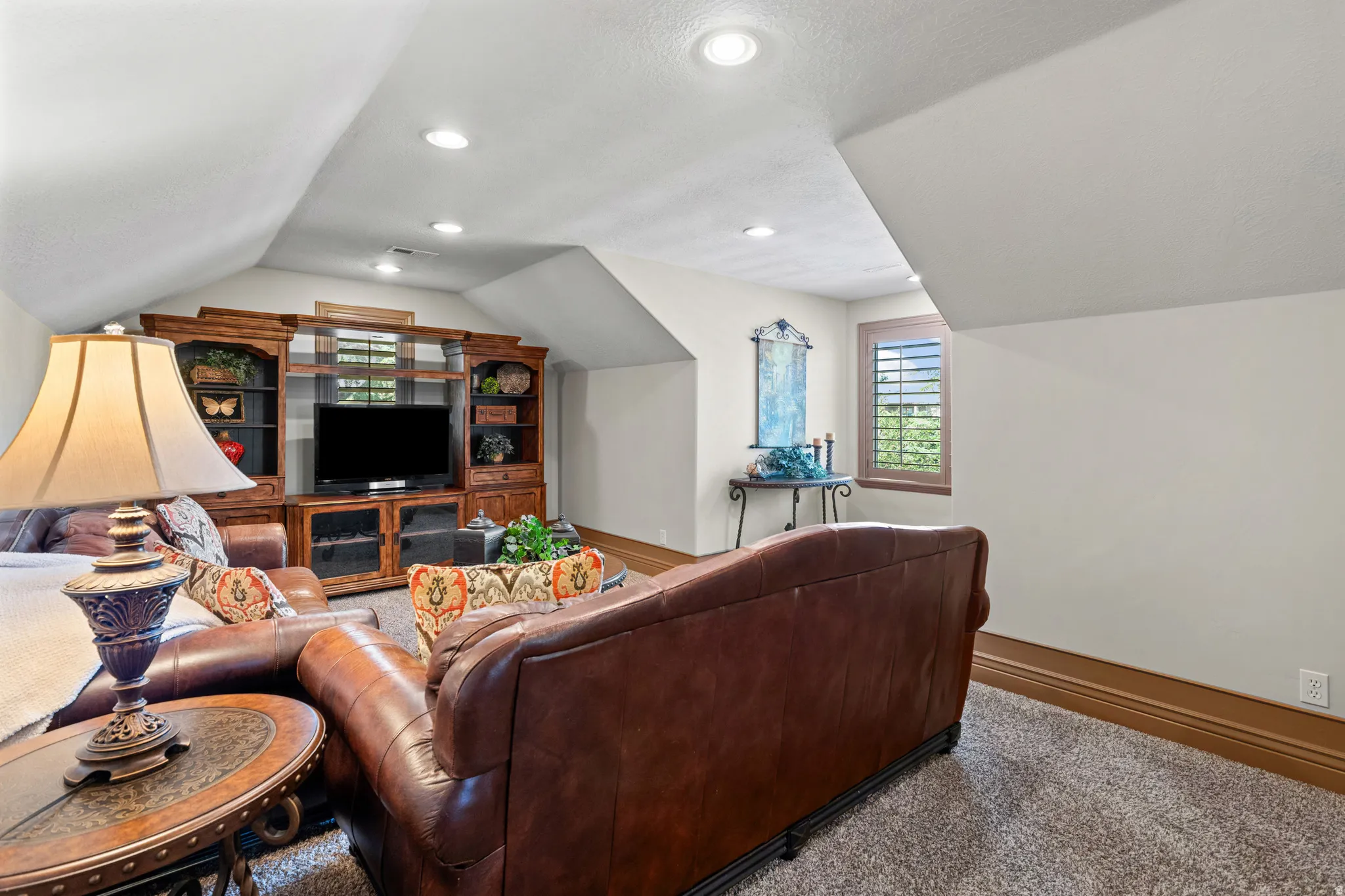 Carpeted room featuring a built-in entertainment center with shelving and cabinetry, recessed ceiling lighting, a window with plantation shutters, and a wall-mounted console table