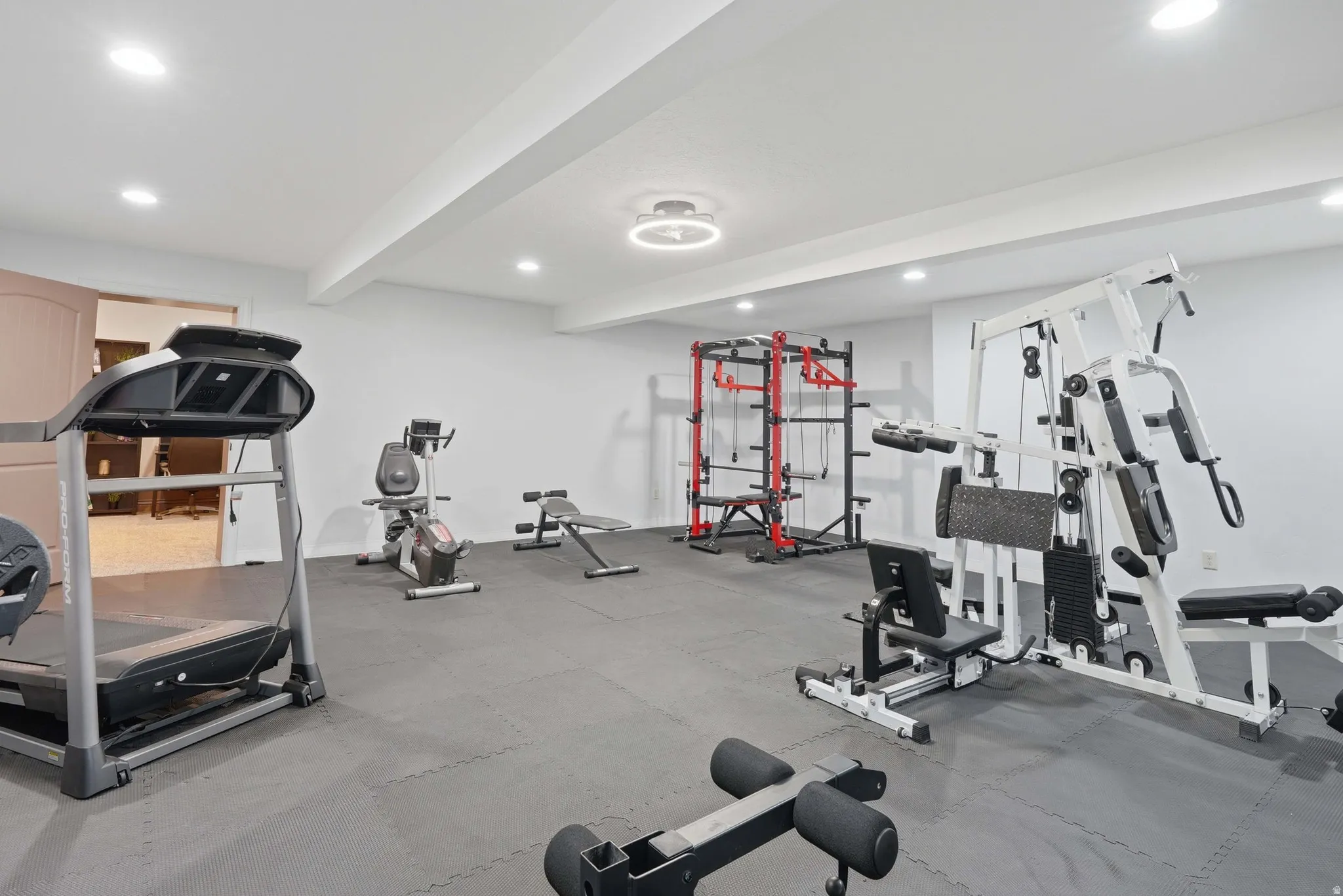 Spacious room featuring gray interlocking floor mats, recessed lighting, a modern circular ceiling light fixture, and white painted walls