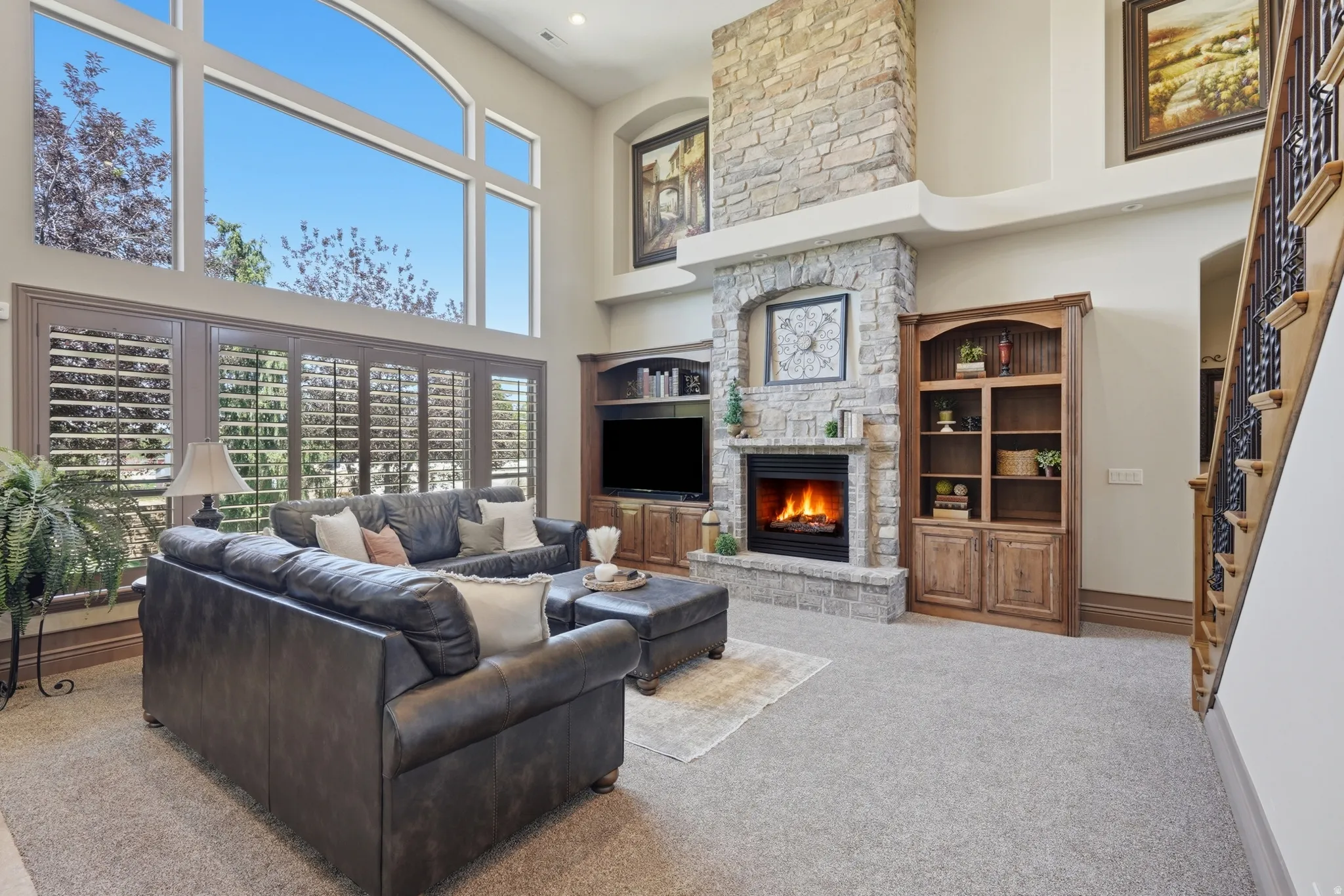 Great room featuring a two-story stone fireplace, built-in media center, and custom plantation shutters