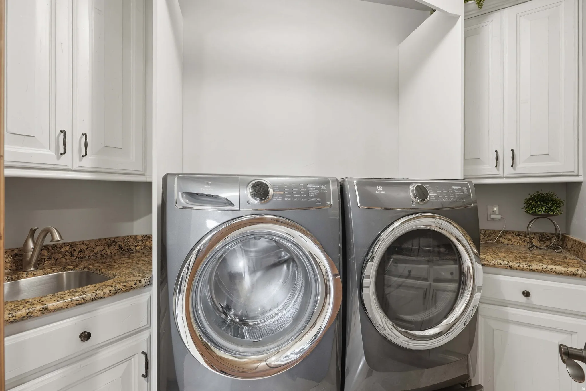 Utility space featuring white shaker-style cabinetry, granite countertops, and a built-in stainless steel sink with a brushed nickel faucet