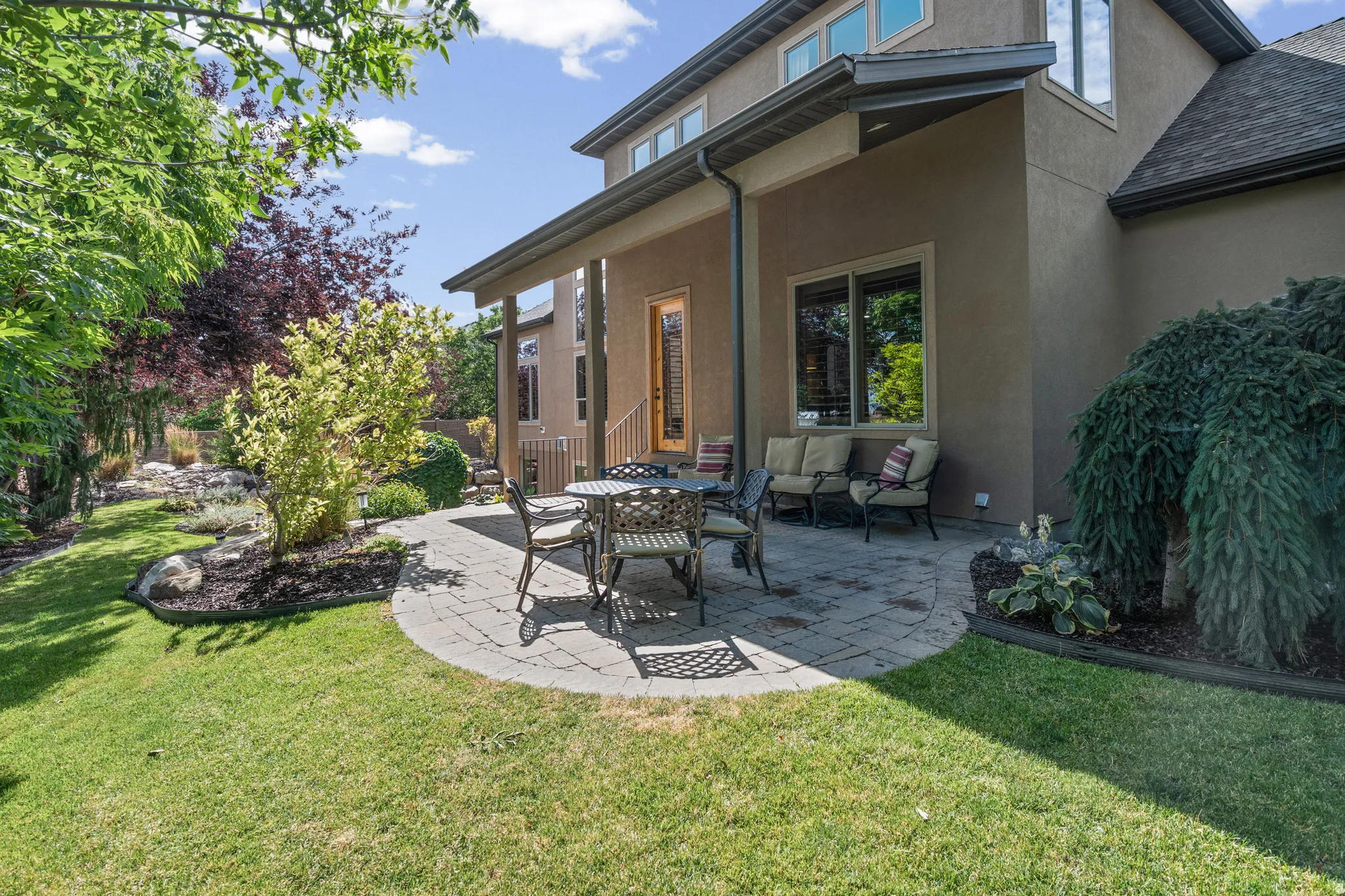 Spacious backyard featuring a curved paver patio, established landscaping, and a manicured lawn