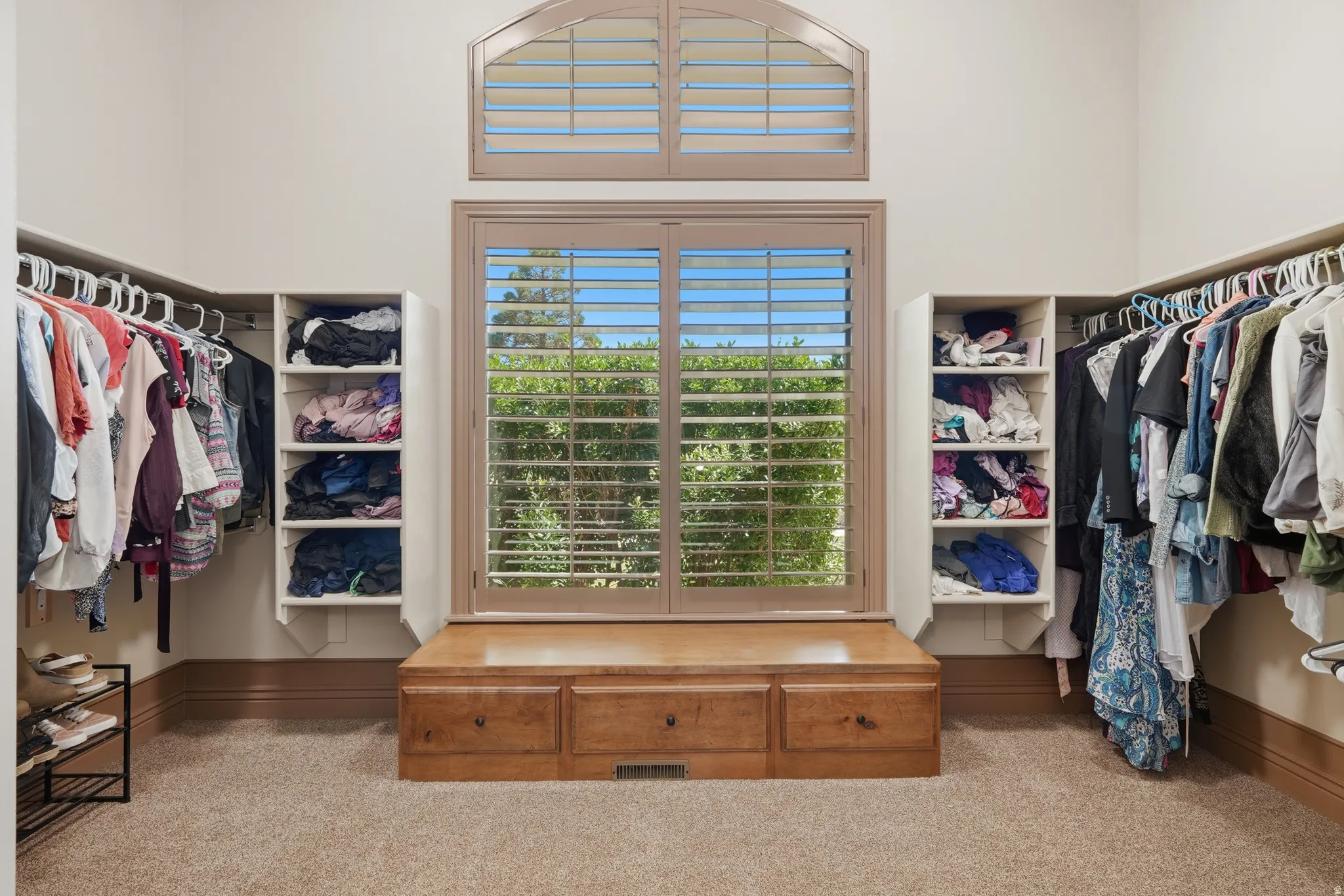 Walk-in closet featuring carpet flooring, built-in shelving, hanging rods, and a window seat with integrated storage drawers