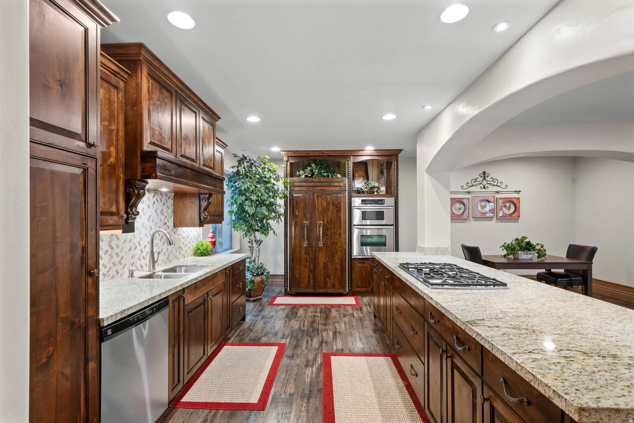 Gourmet kitchen featuring extensive custom wood cabinetry, granite countertops, stainless steel appliances including a built-in oven and microwave, a gas cooktop on the island, and wood-finish flooring