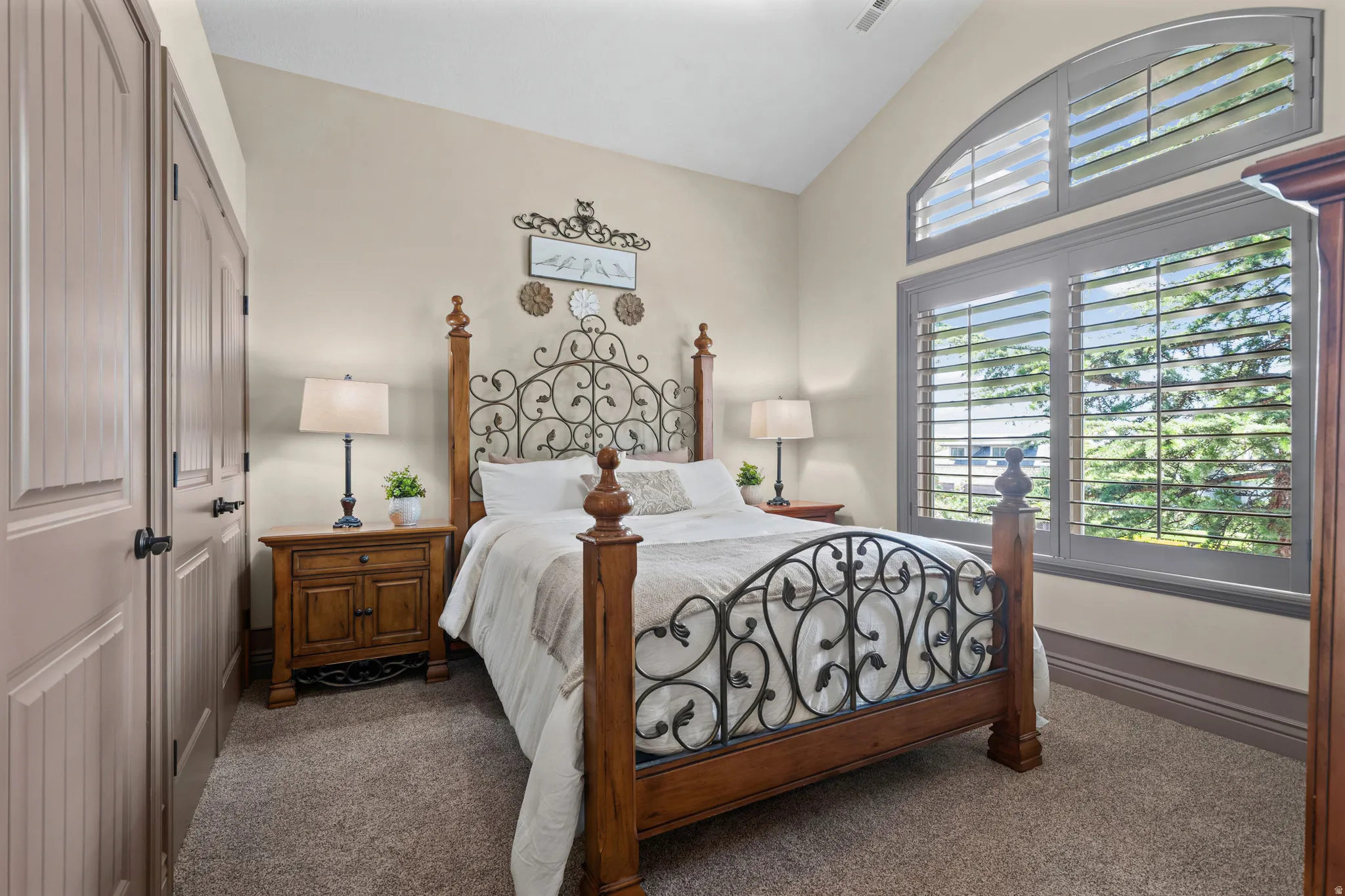 Vaulted ceiling room featuring a large arched window with plantation shutters, two panel-style doors, and carpeted flooring