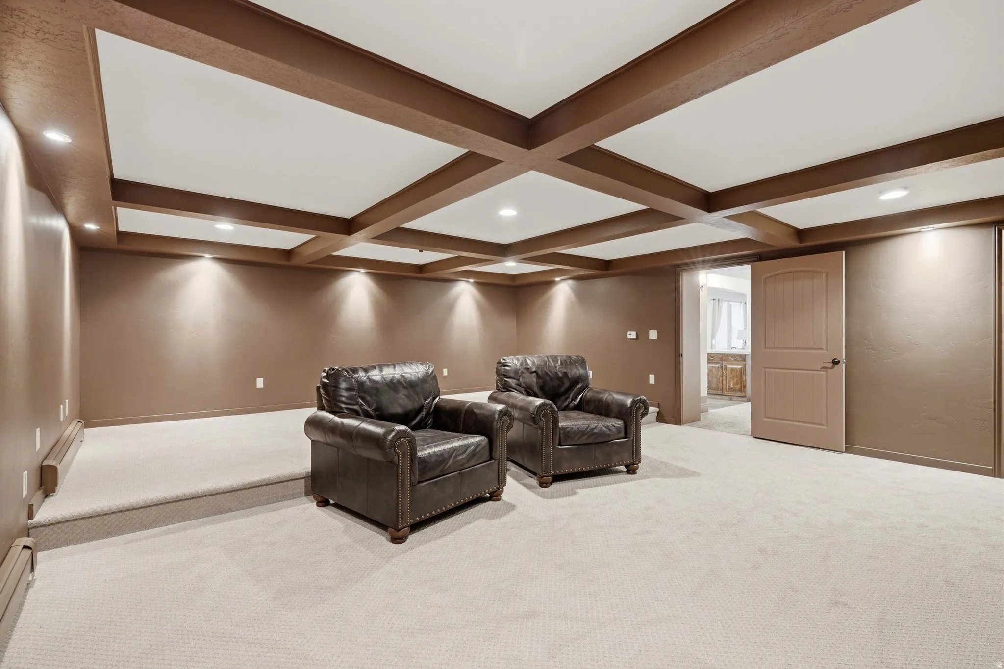 Spacious recreation room featuring a coffered ceiling with recessed lighting, wall sconces, and neutral carpeting