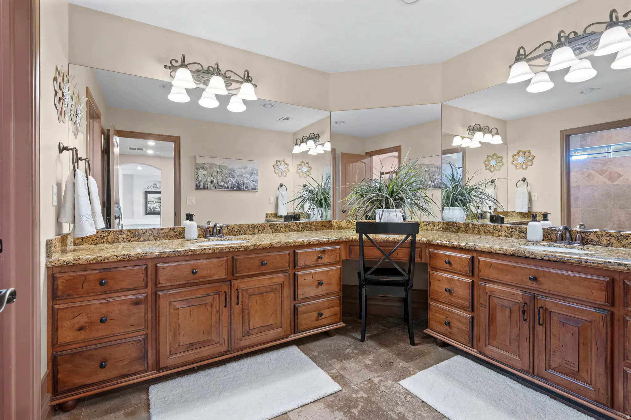 Dual sink vanity featuring granite countertops, wood-finish cabinetry, and expansive wall-mounted mirrors