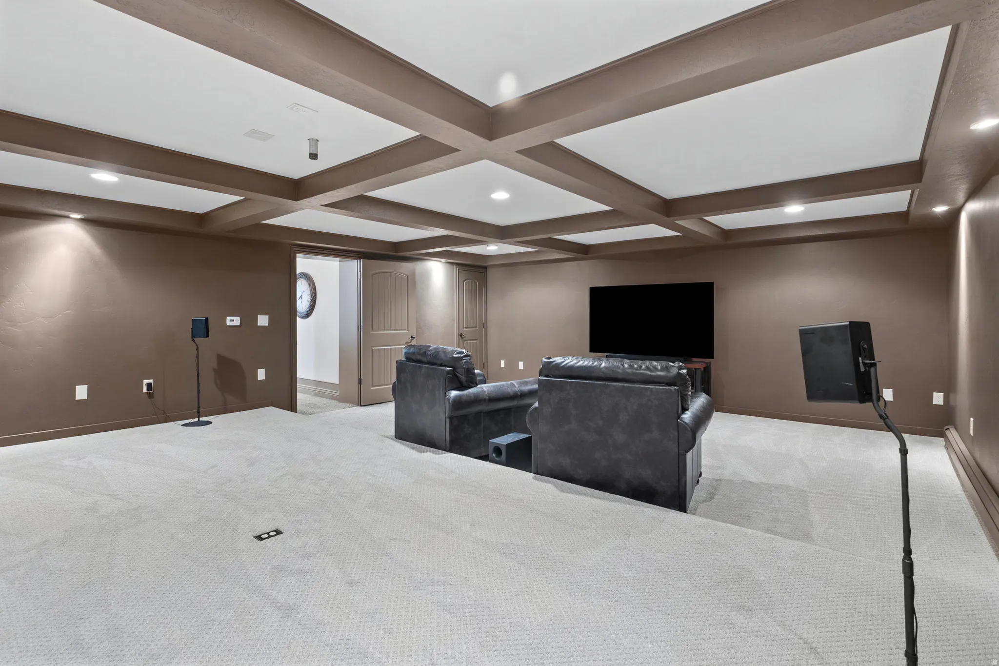Spacious media room featuring a coffered ceiling, recessed lighting, and wall sconces