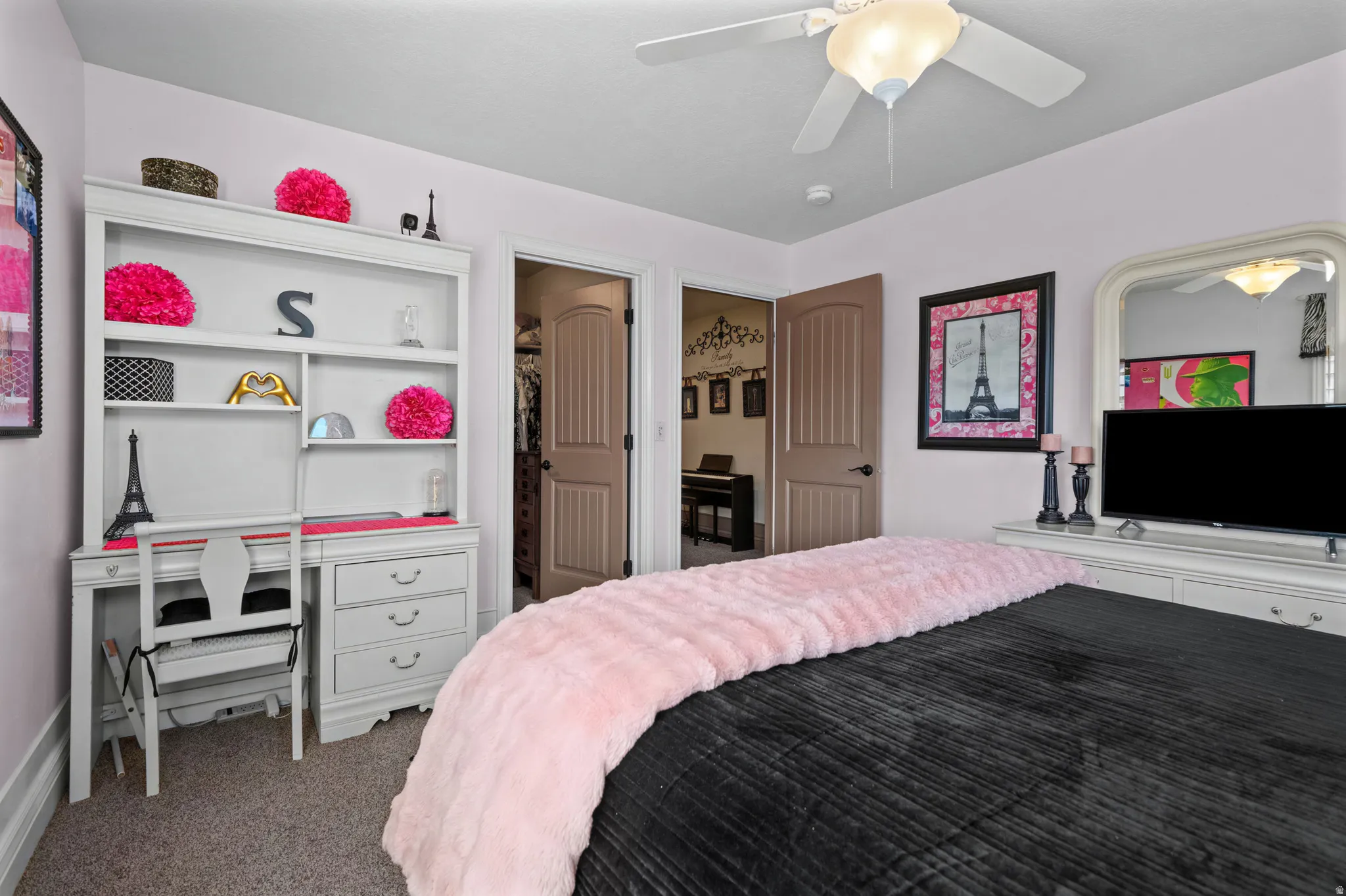 Bedroom featuring light pink walls, carpet flooring, a ceiling fan with integrated lighting, and a white built-in desk with shelving