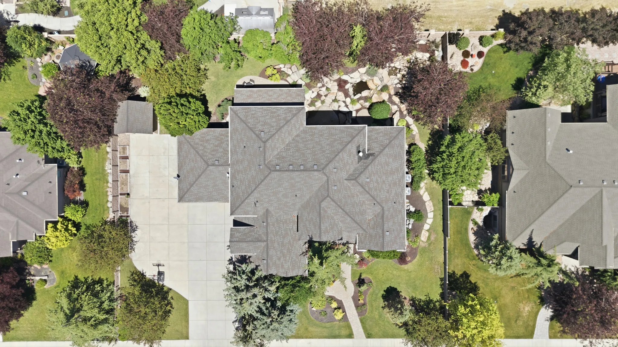 Spacious property featuring a large asphalt shingle roof, extensive concrete driveway, RV parking, and mature landscaping