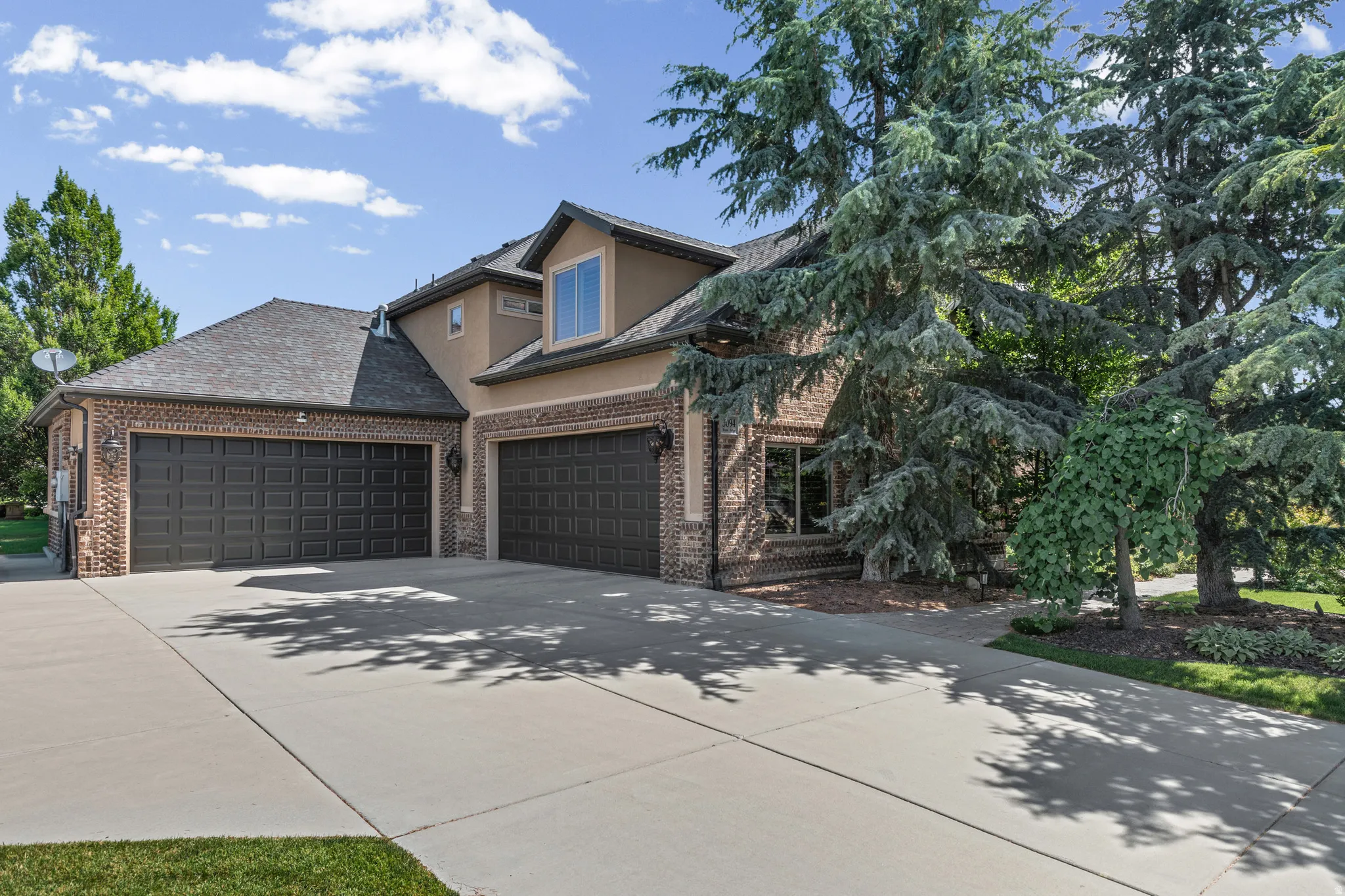 Brick and stucco exterior featuring two attached garages with dark paneled doors, a concrete driveway, and mature landscaping