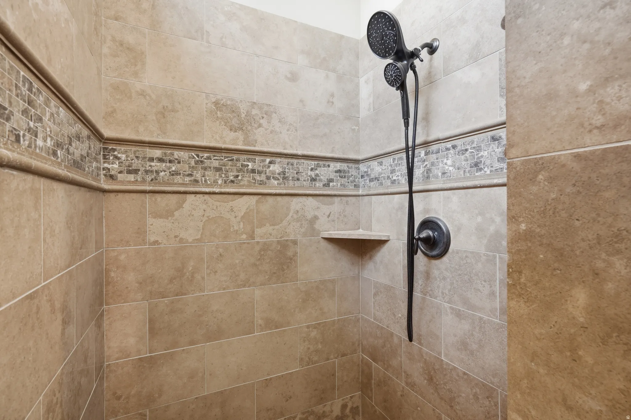 Tiled shower stall featuring a mosaic accent band, corner shelf, and oil-rubbed bronze shower fixtures