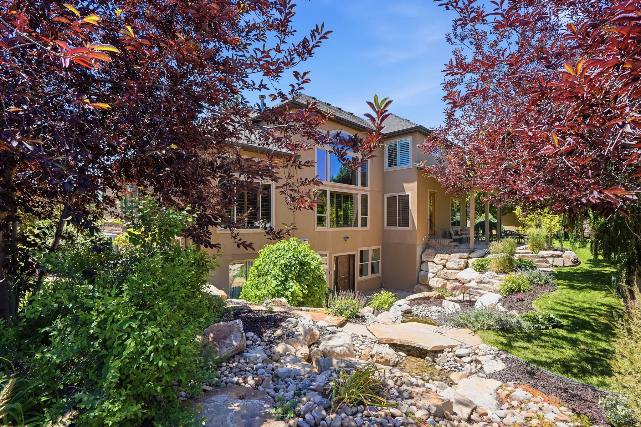 Terraced backyard featuring rock gardens, a flowing water feature, and mature red-leaf trees